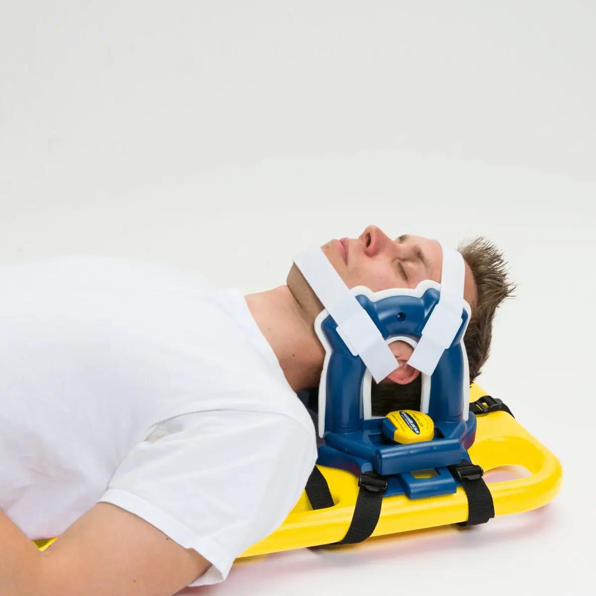 Eine Person liegt auf einer Trage, der Kopf wird mit der Kopffixierung für Spineboard aus abwaschbarem, latexfreiem HDPE stabilisiert.