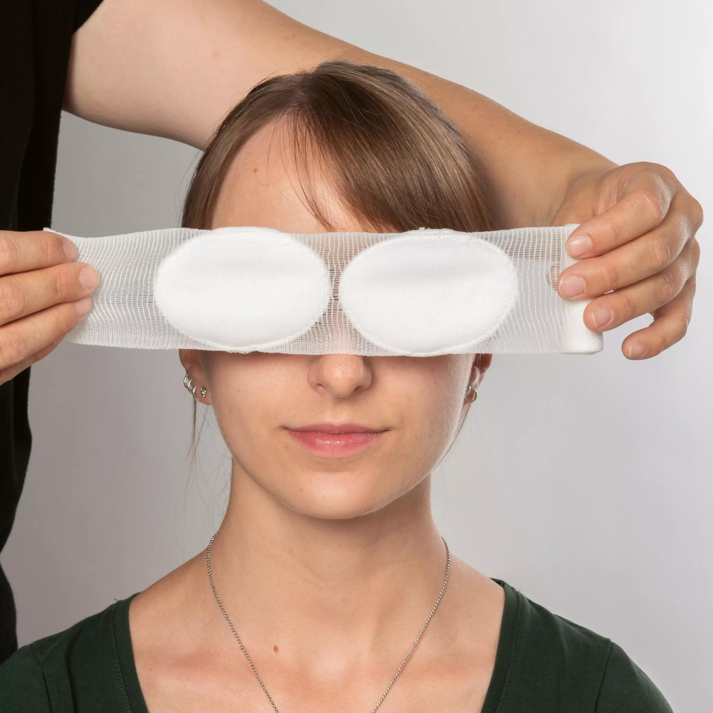 Eine Person mit grünem Hemd hält sich zwei weiche, ovale Werola® Augenverband Pads sanft und druckfrei über beide Augen.