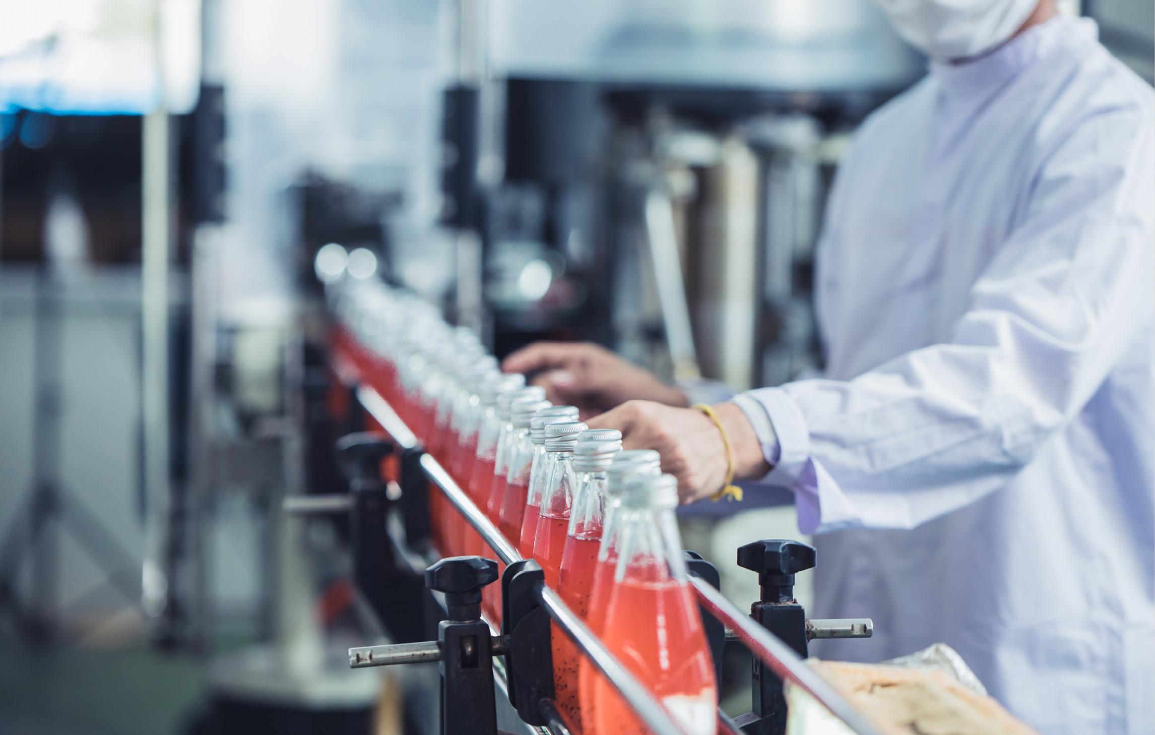 Eine Abfüllanlage für Limonade. Eine Mitarbeitender in weißem Kittel kontrolliert die Flaschen