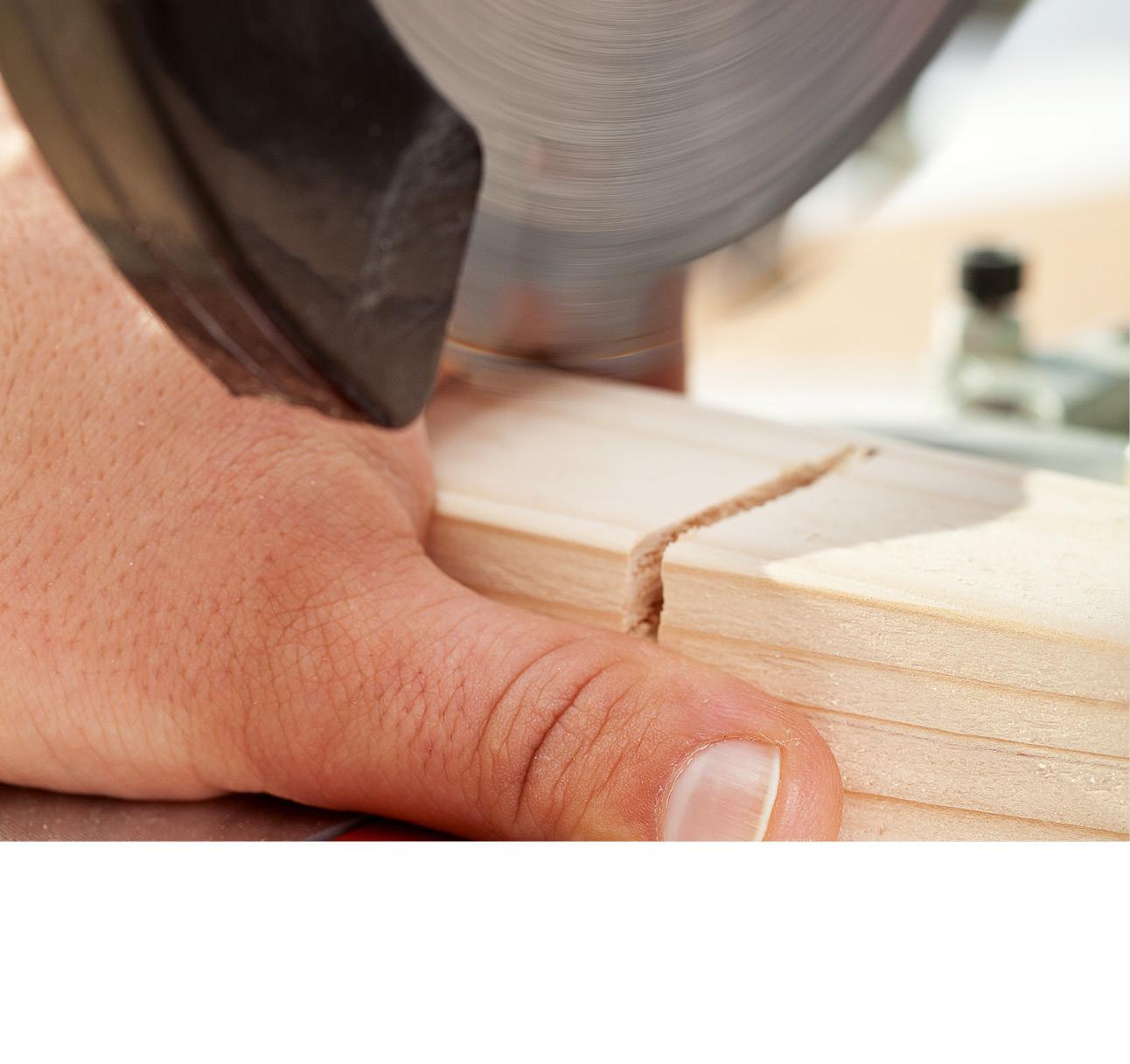 Eine Kreissäge in Nahaufnahme. Sie schneidet ein Stück Holz. Eine Hand ist dem Sägeblatt gefährlich nah.