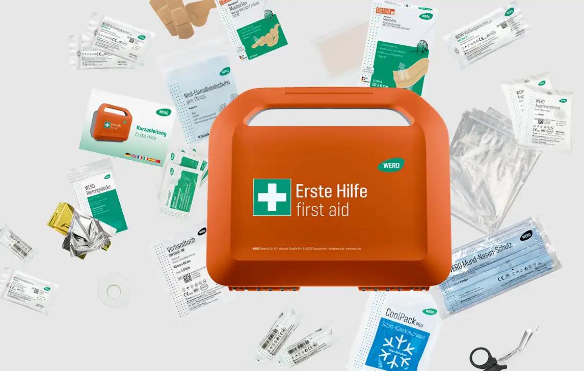 Orange WERO Erste-Hilfe-Kasten mit Kreuzsymbol, umgeben von Verbandsmaterial, Mull, Desinfektionstüchern, Wattestäbchen und Schere.
