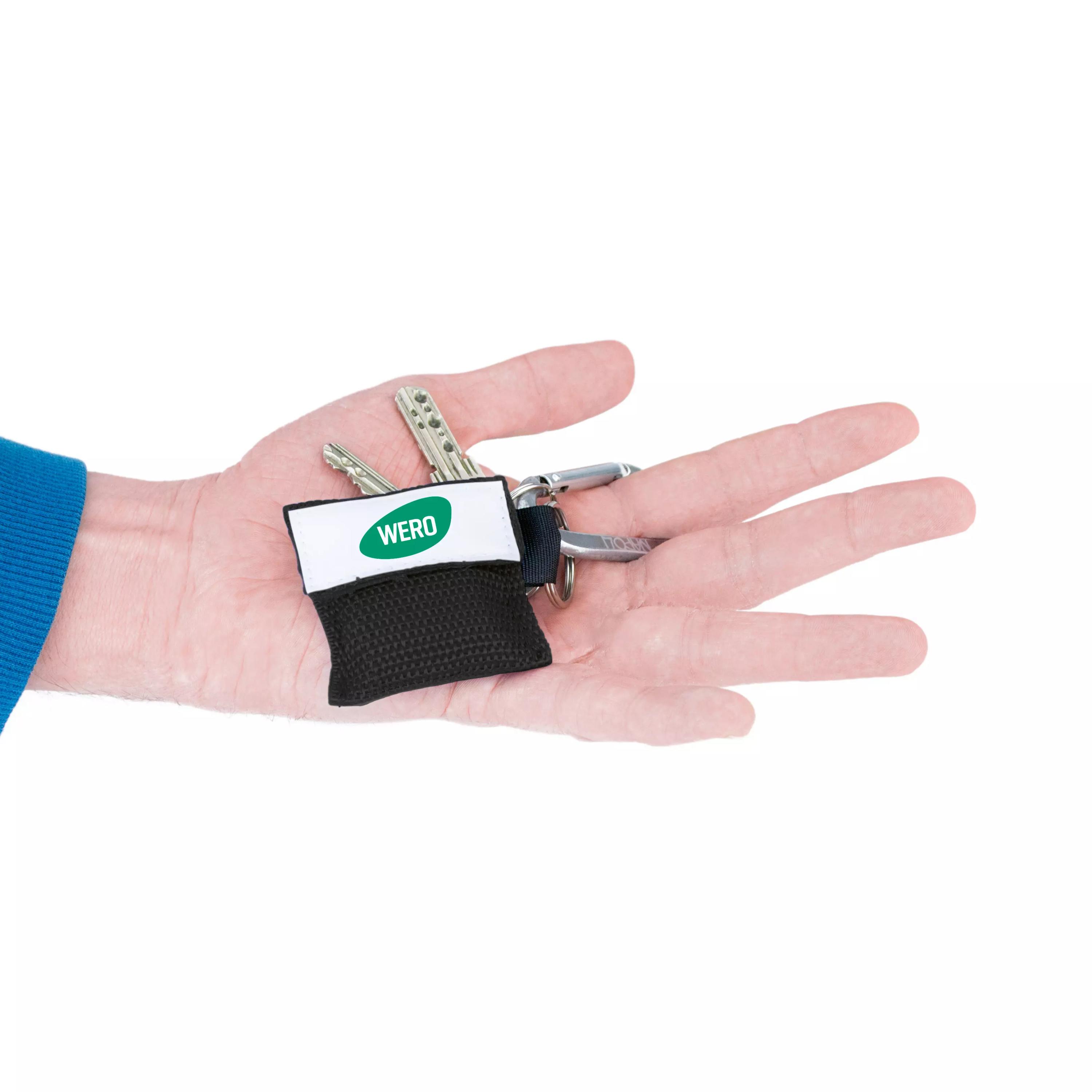 Eine Hand hält ein WERO Beatmungstuch in Schlüsselanhänger, kompakt in schwarzer Nylontasche mit weißem Label, zwei Schlüsseln und Silberkarabiner.