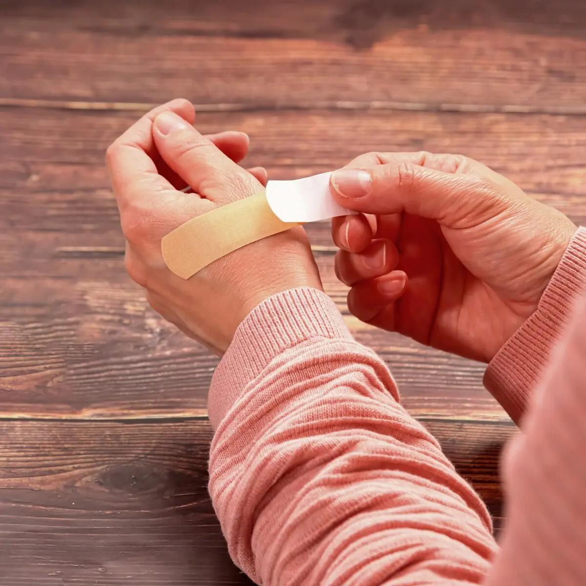 Eine Hand hält ein Pflasterstrips Weroplast® MasterTex - 2,5 cm, 50 Stk, das aus anpassungsfähigem, textilem Gewebe sanft am Handgelenk befestigt wird.