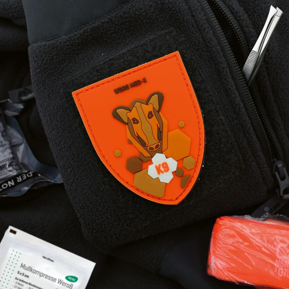 Patch WERO MED-X® K9 Hunter Medic Pack mit stilisiertem Tierkopf, K9-Schriftzug und farbigen Details an einer Jacke befestigt.