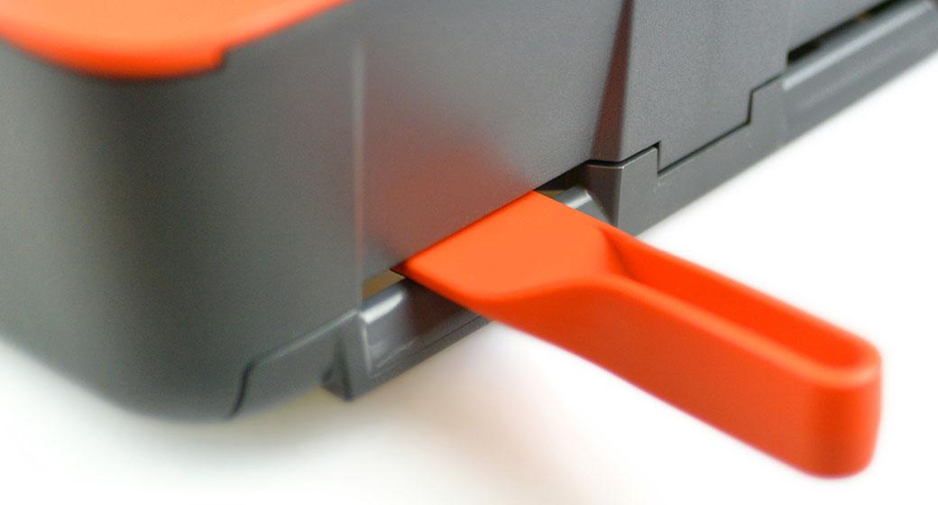 Graues und orangefarbenes Multifunktionsgerät mit schwarzer Klappe und seitlichem orangefarbenem Griff, aus erhöhter Perspektive fotografiert.