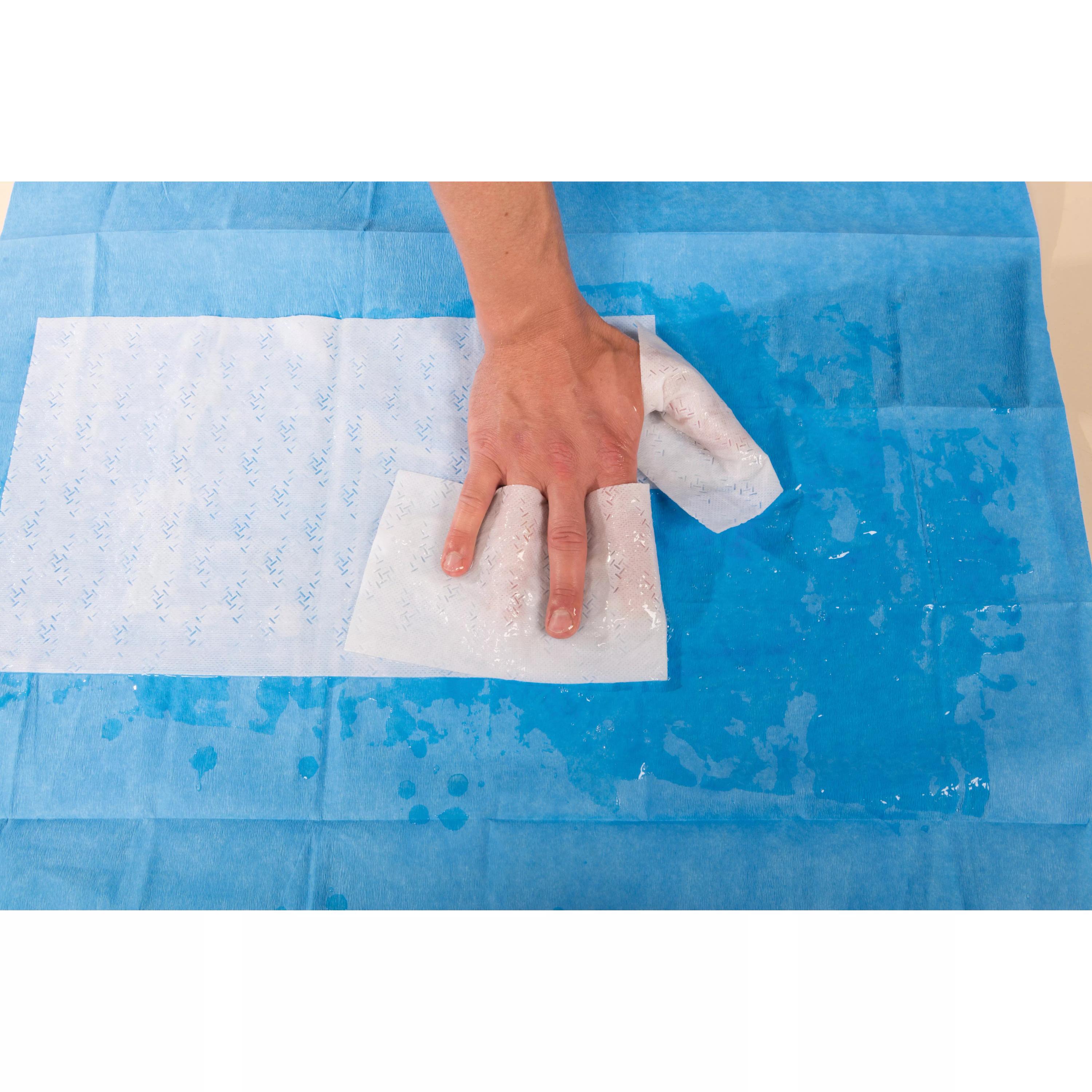 Eine Hand wischt mit einer weißen WATER-JEL® HA First Responder Handkompresse, steril, Feuchtigkeit von einer blauen, weichen Oberfläche.