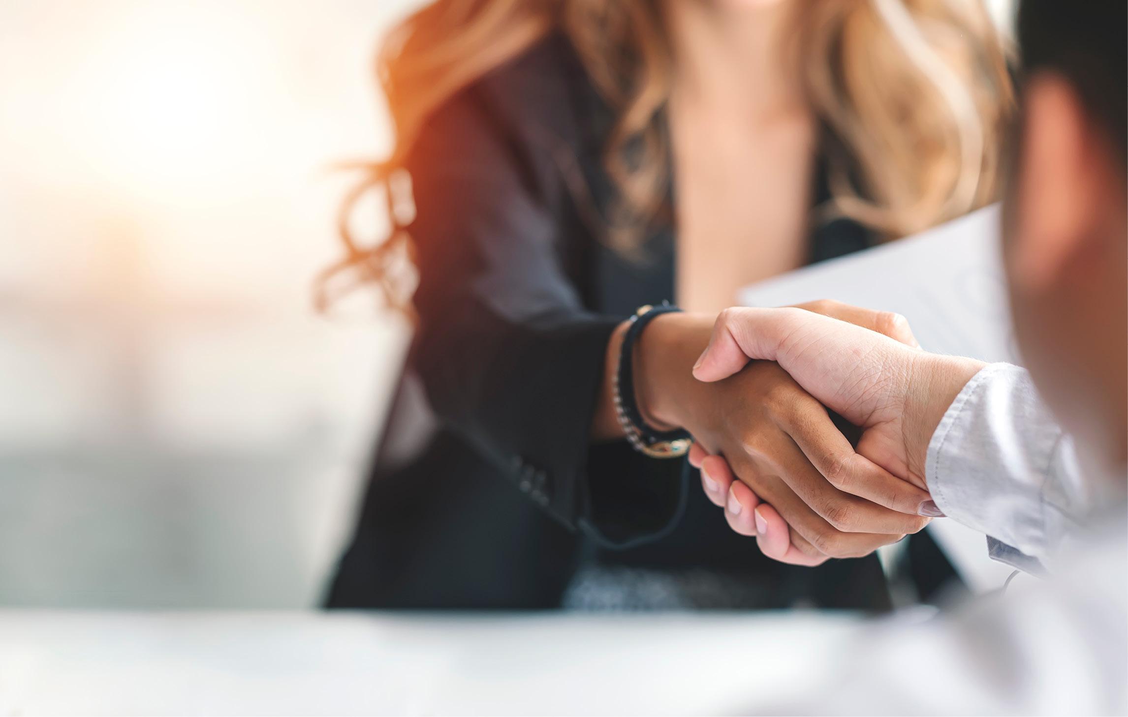 Zwei Personen schütteln sich die Hand. Sie tragen Business-Kleidung