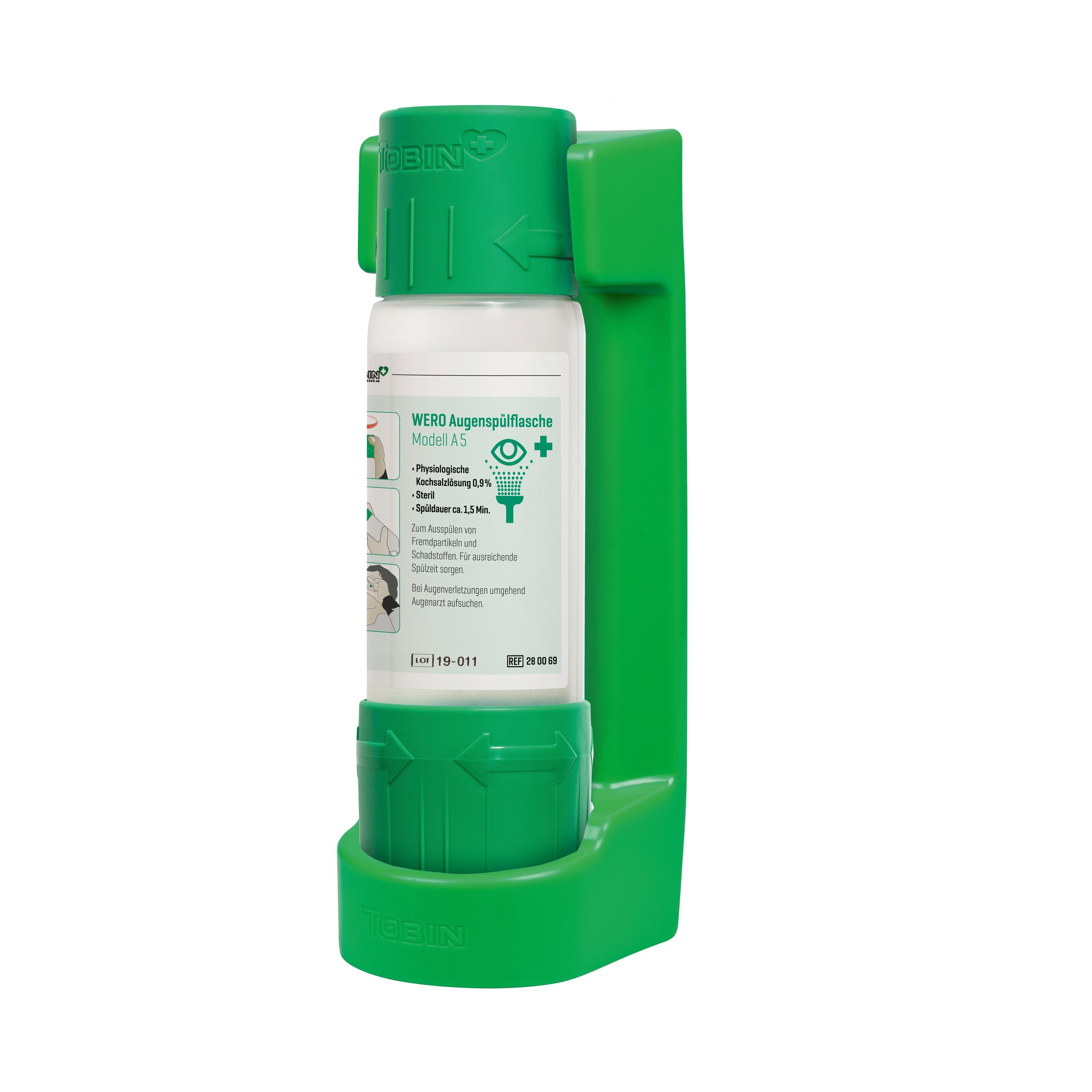 WERO Augenspülflasche Modell A 5 steht mit weißem Kunststoffdeckel und rotem X in grüner Wandhalterung, seitlich ist ein beschriftetes Etikett angebracht.