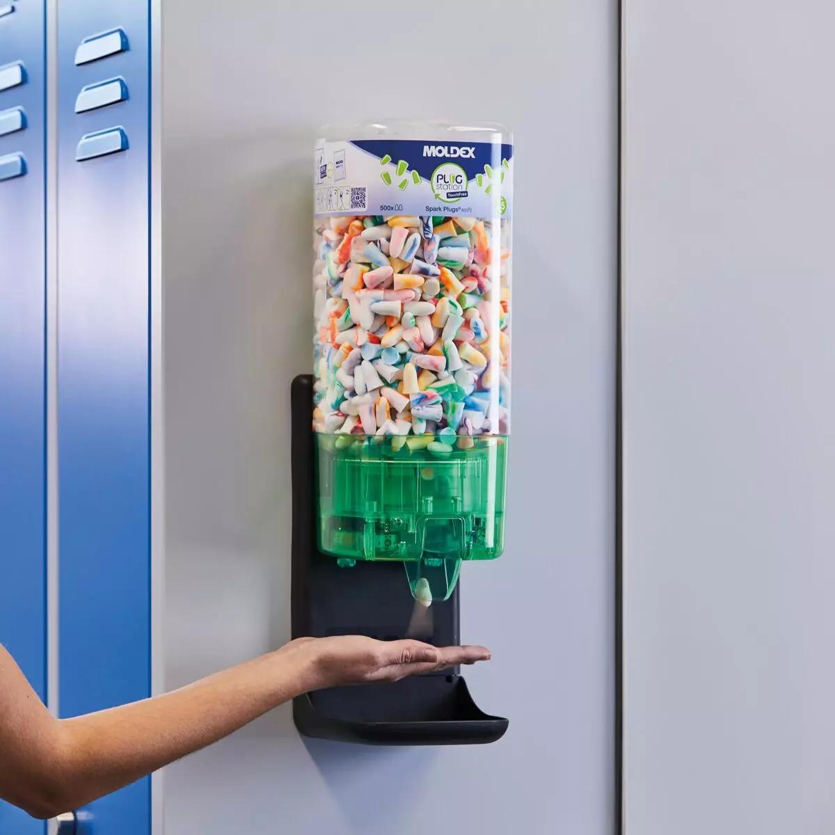 Eine Hand nähert sich dem MOLDEX TouchFree Spendermechanismus für Gehörschutzspender mit bunten Ohrstöpseln zur hygienischen, berührungslosen Entnahme.