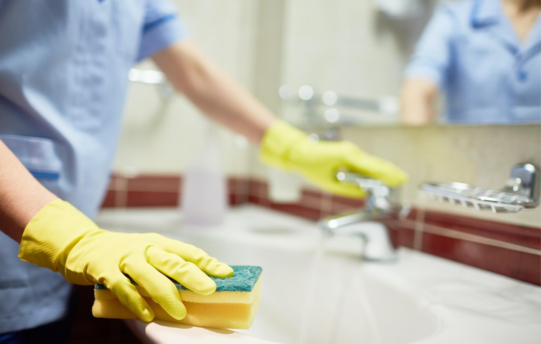 Eine Reinigungskraft mit gelben Gummihandschuhen reinigt ein Waschbecken