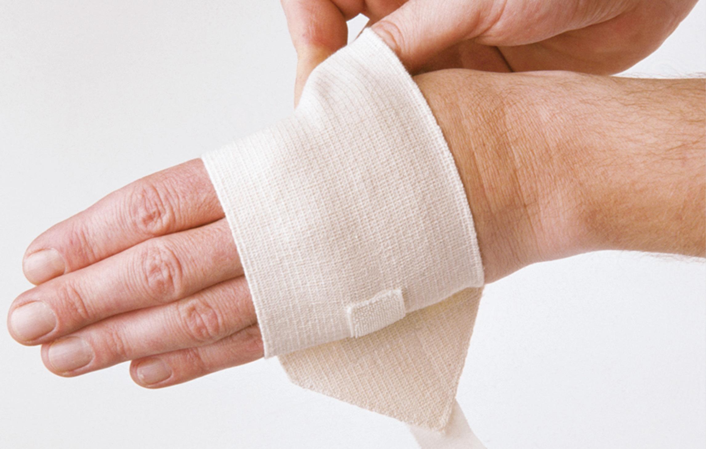 Eine Person zieht sich eine hellbeige Handbandage über den Handrücken