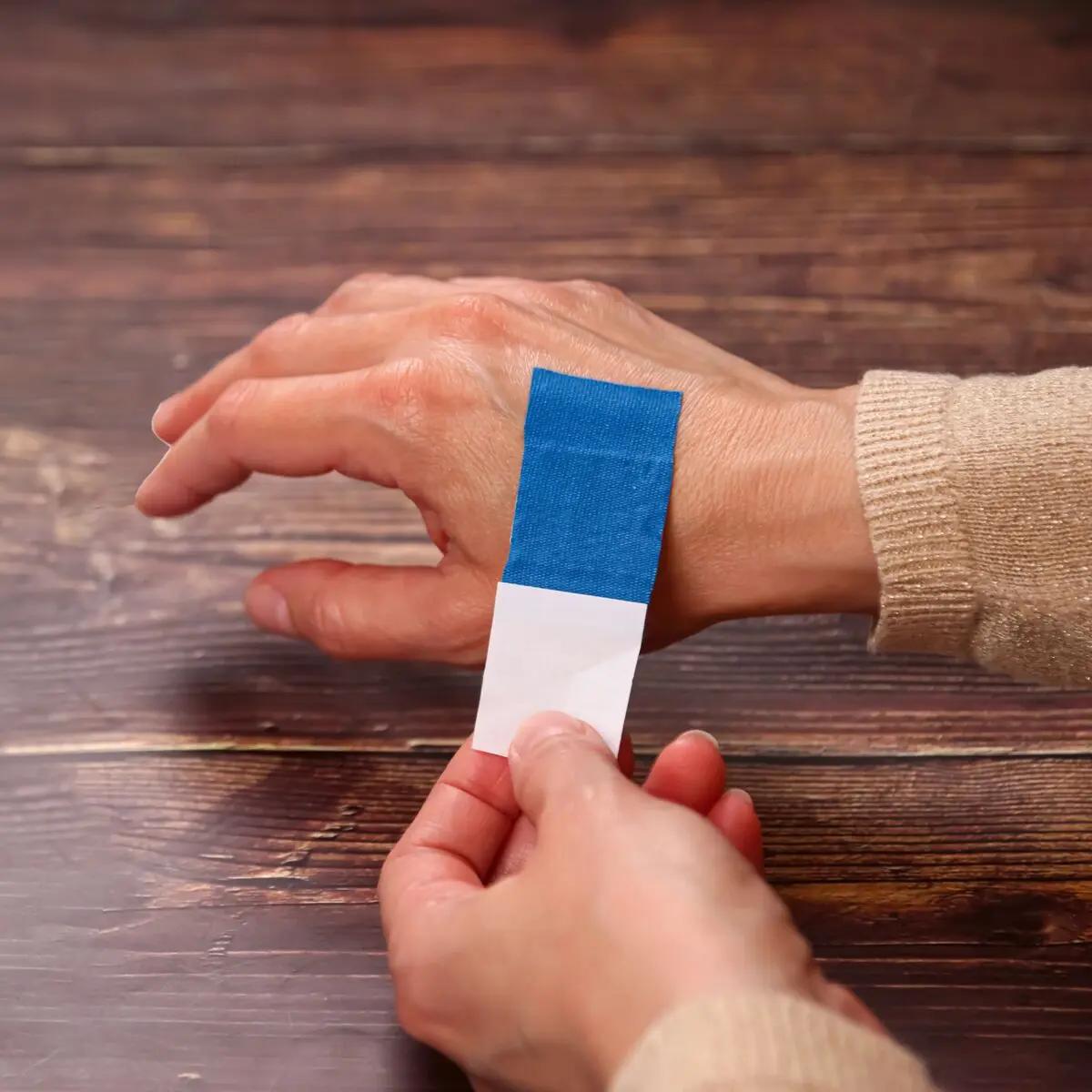 Eine Hand drückt einen Wundschnellverband Weroplast® PowerDetect mit blauer, detektierbarer Beschichtung und längs- sowie querelastischem Gewebe sanft auf den Ringfinger.