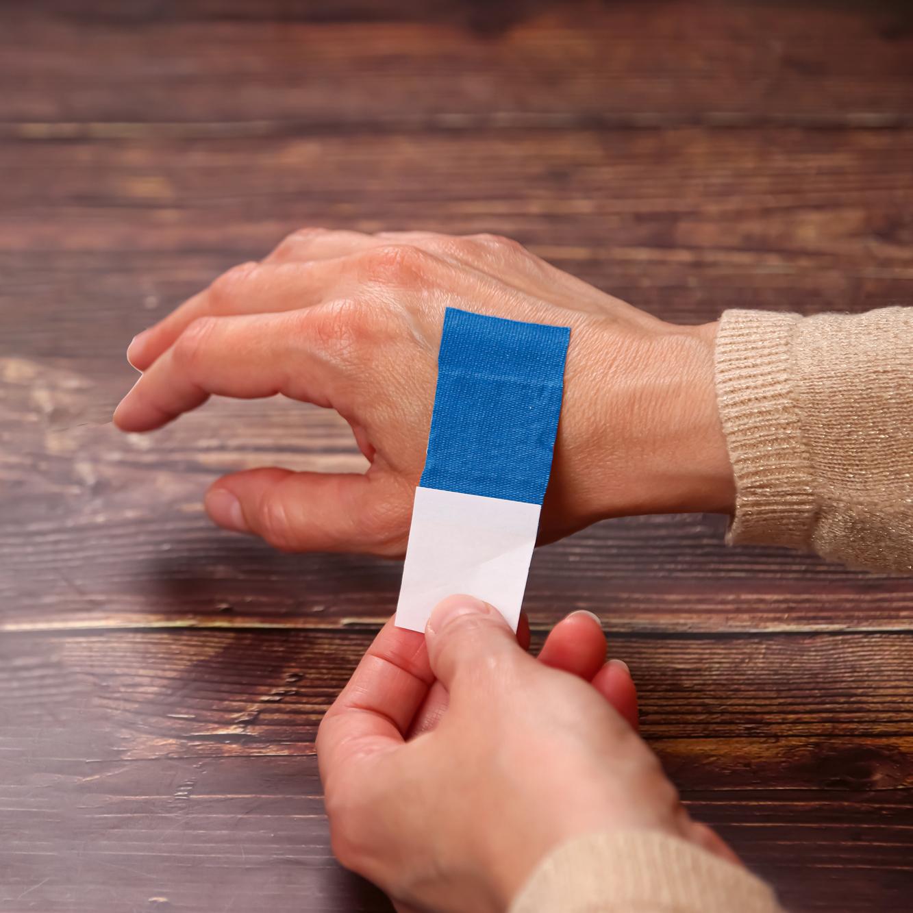 Eine Hand drückt einen Wundschnellverband Weroplast® PowerDetect mit blauer, detektierbarer Beschichtung und längs- sowie querelastischem Gewebe sanft auf den Ringfinger.