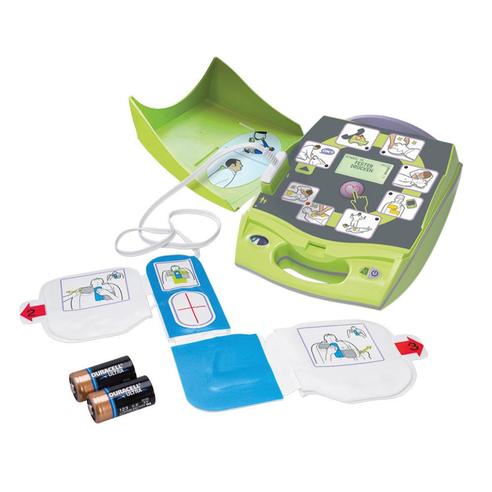 Grünes mobiles AED-Gerät mit geöffneter Konsole, Anzeige, blauer Defibrillationselektrode und zwei Duracell-Batterien daneben