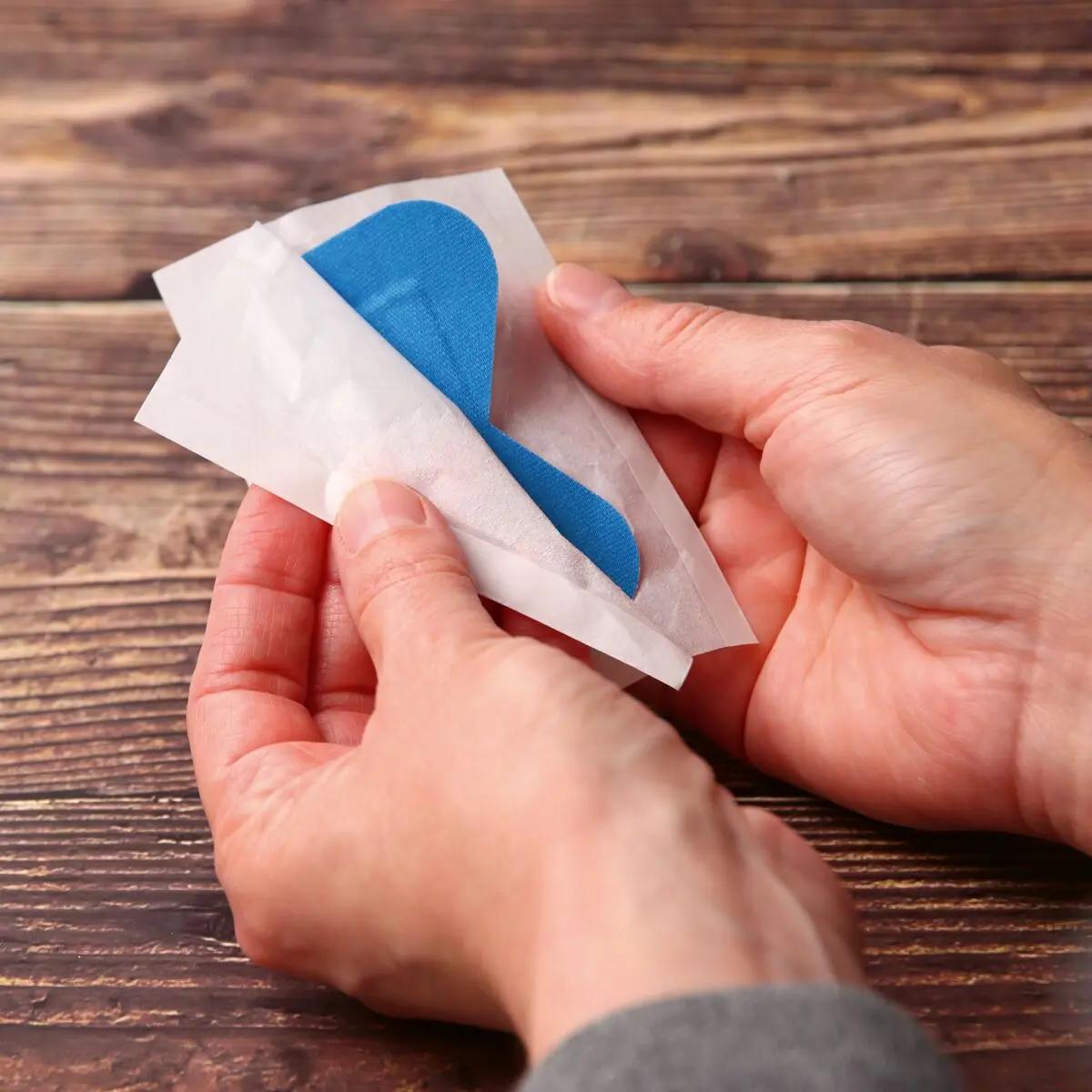 Zwei Hände lösen ein leuchtend blaues Pflaster aus dem Pflasterset Weroplast® PowerDetect - Perfect Mix aus seiner weißen Hülle, das detektierbar und elastisch ist.