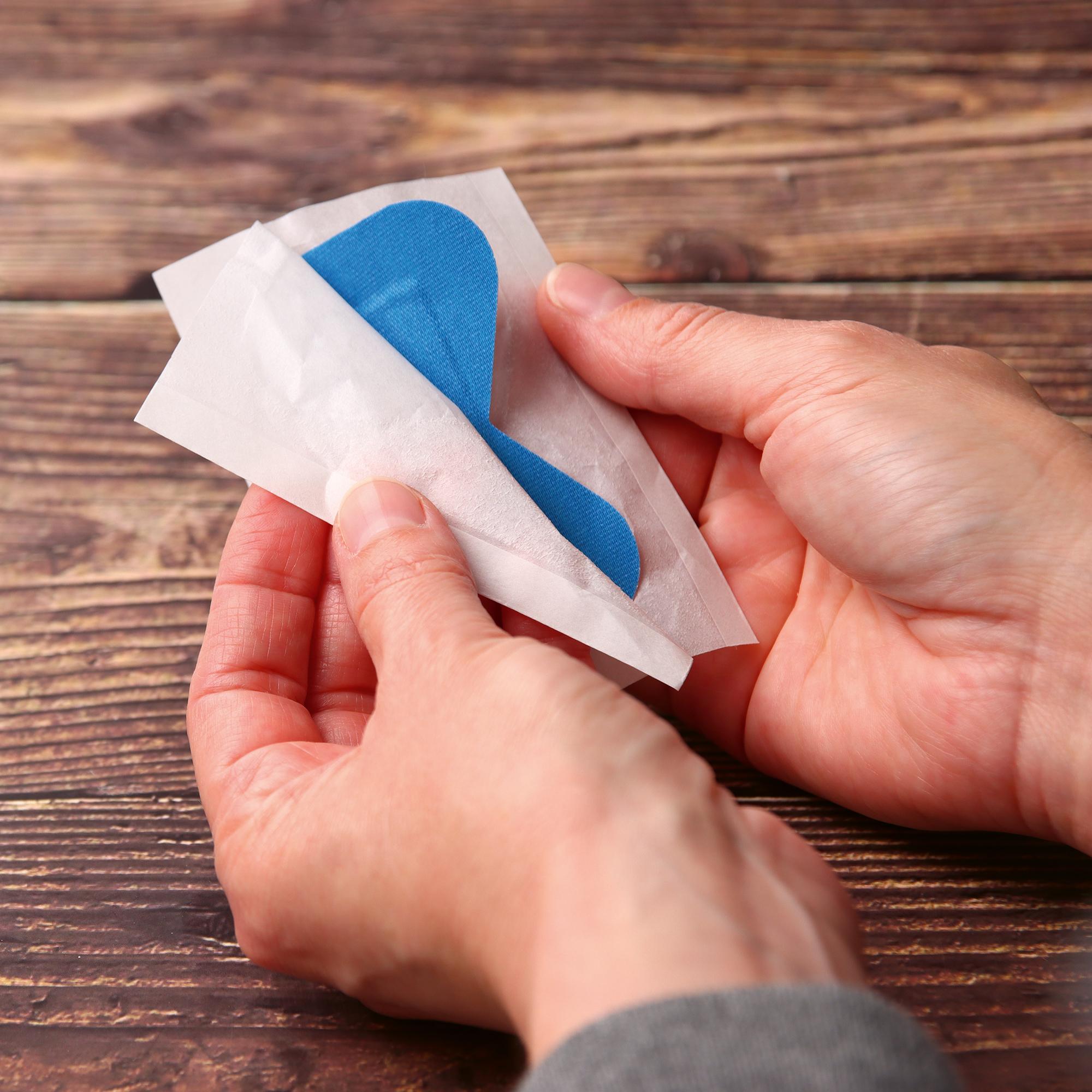 Zwei Hände lösen ein leuchtend blaues Pflaster aus dem Pflasterset Weroplast® PowerDetect - Perfect Mix aus seiner weißen Hülle, das detektierbar und elastisch ist.