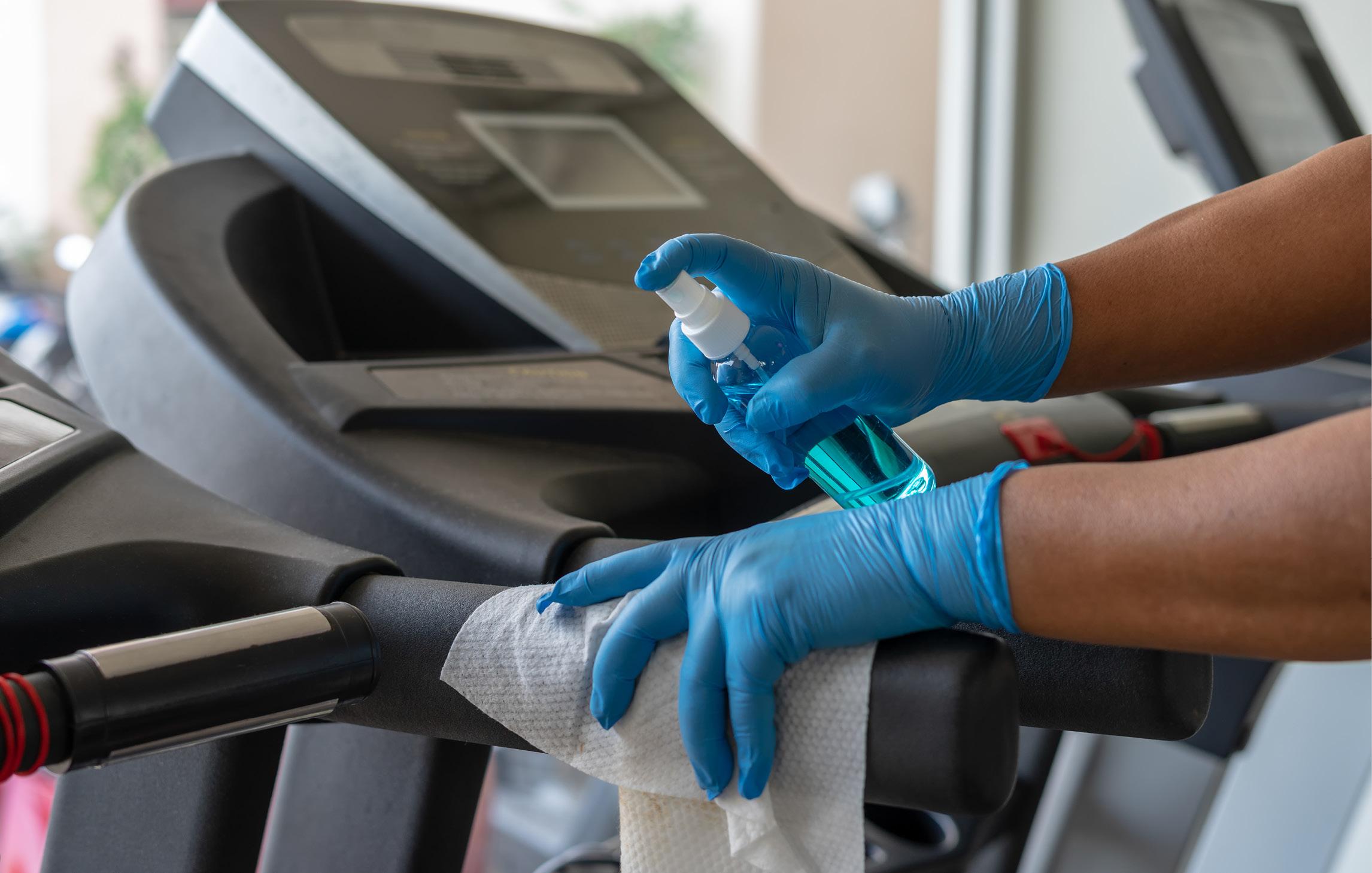 Ein Fitnessgerät wird desinfiziert. Die Person trägt blaue Einmalhandschuhe