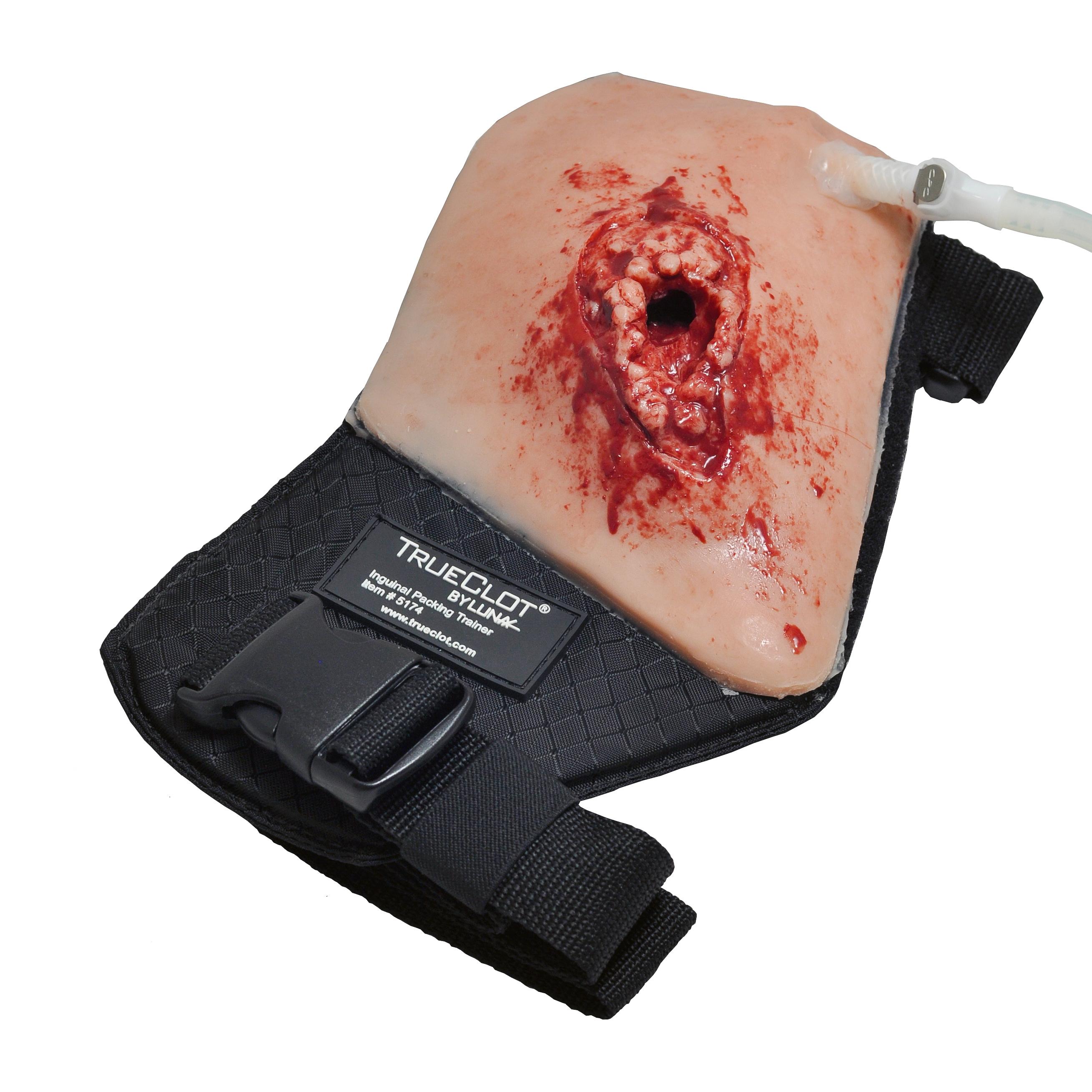 Ein TrueClot® Leisten Wound Packing Trainer mit simulierter Leistenwunde, blutähnlichem Inhalt und schwarzem Befestigungsriemen für realistische Trainings.