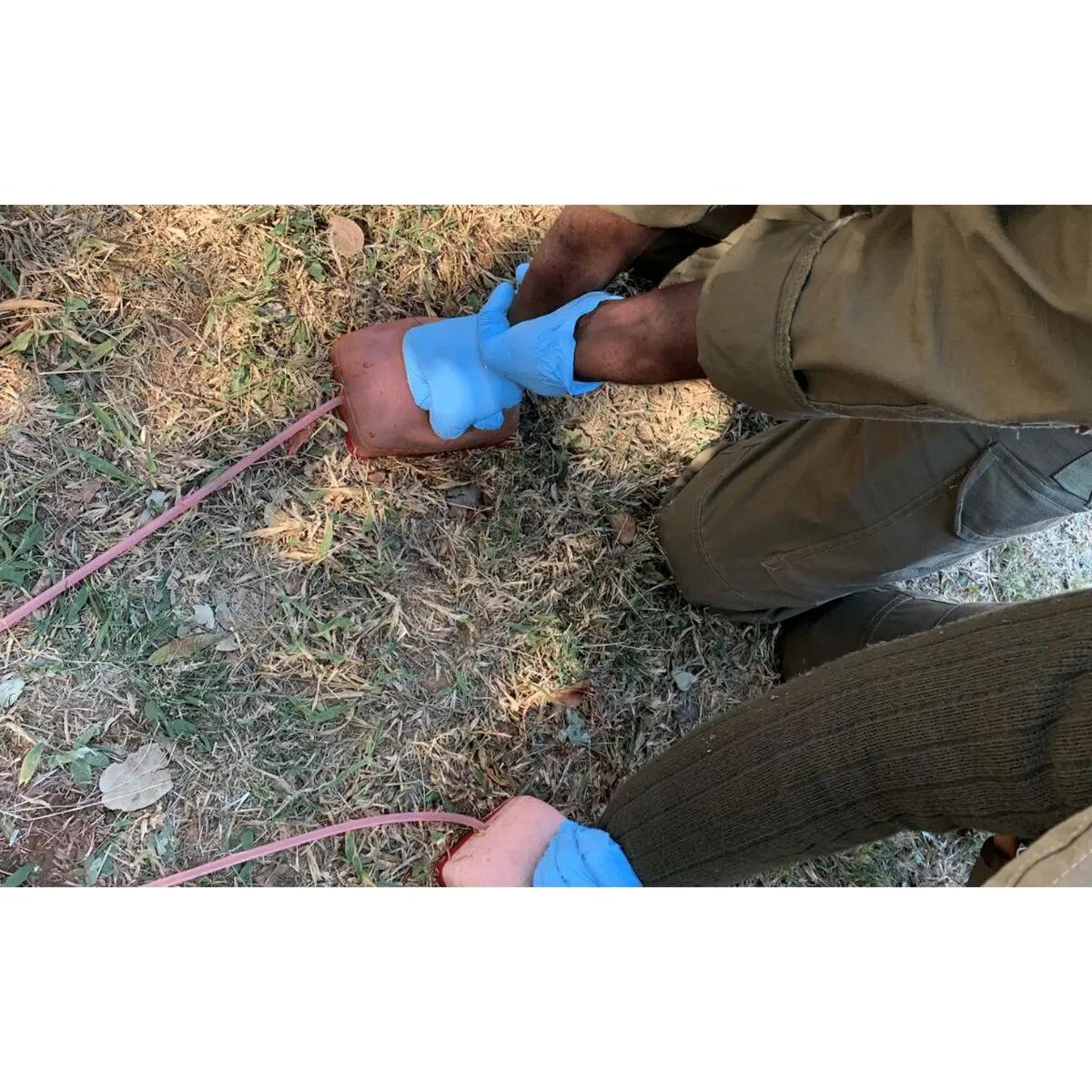 Zwei Personen in grüner Kleidung üben am Battlefield Partners Wound Packing Trainer mit orangefarbenem Einsatz und rosa Schlauch eine realistische Wundversorgung.