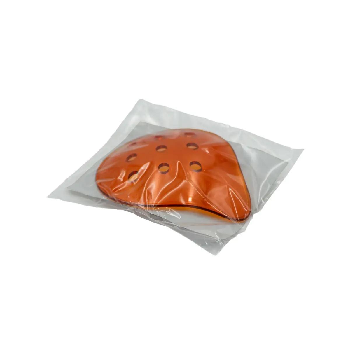 Ein gewölbter, orangefarbener Lifeguard Polycarbonate Eye Shield mit sechs seitlichen Öffnungen liegt in einer transparenten Kunststoffverpackung.