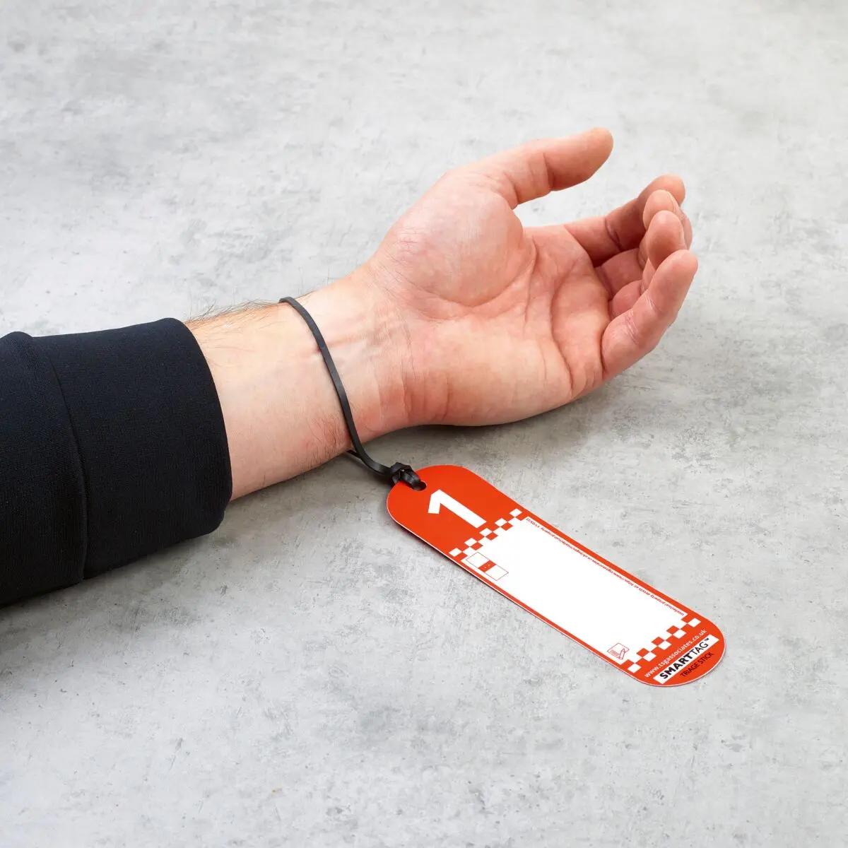 Ein Arm mit angelegtem SmartTriage™ First Response - Anhängekarten-Set, das eine auffällige rot-weiße Triagekarte mit Checkered-Muster am Handgelenk zeigt.