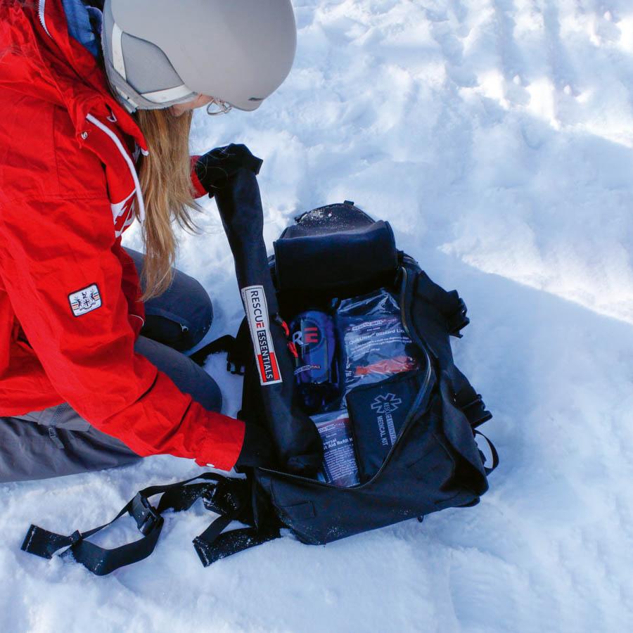 Eine Person in roter Jacke öffnet im Schnee einen Rucksack mit der Slishman Traction Splint (STS), einer kompakten, leicht anpassbaren Schiene.