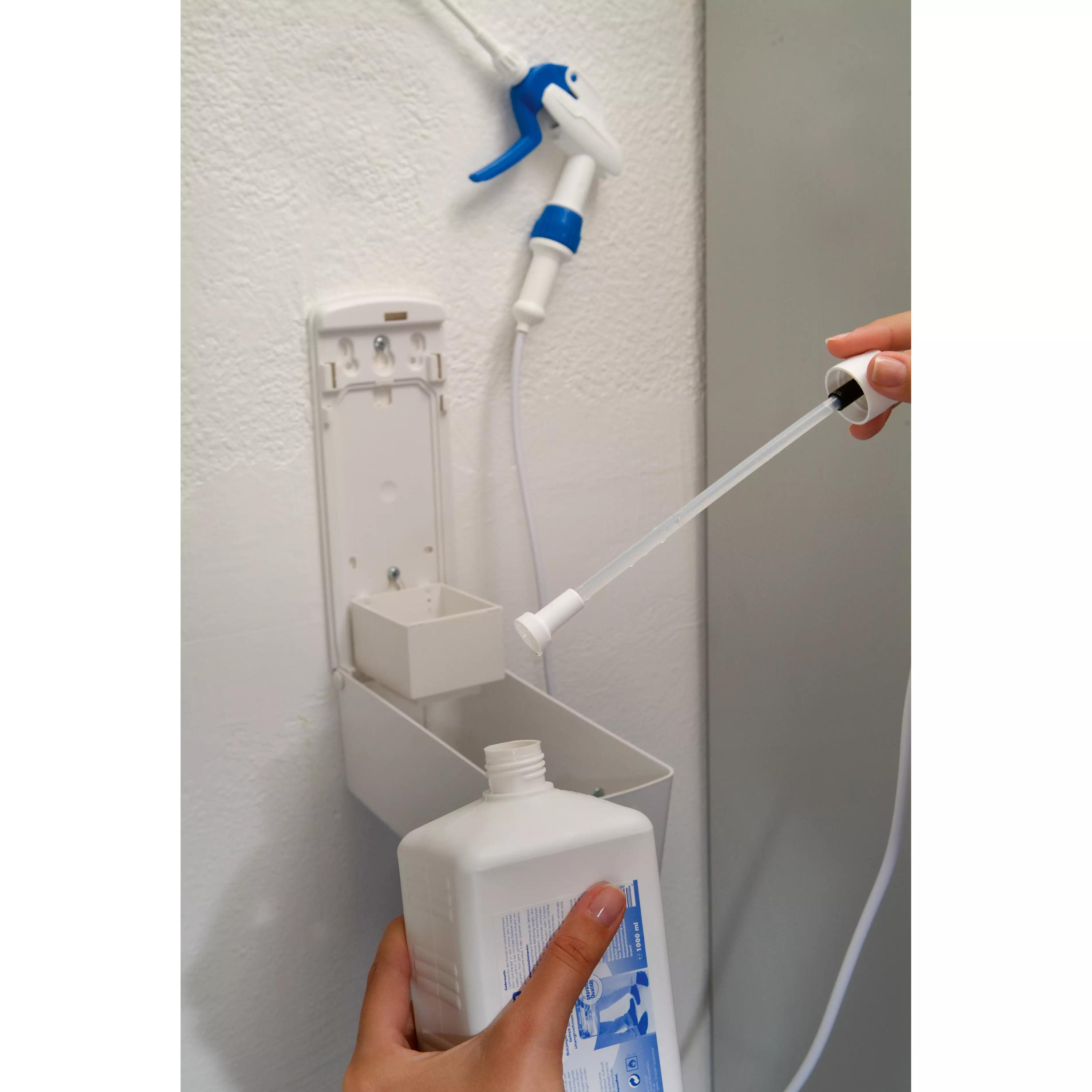 Ein Pedexan® Schuhdesinfektionsmittelspender mit 1,4 m Sprühlanze wird mit einer weißen Flasche an einem Wandspender und blauem Sprayzubehör nachgefüllt.