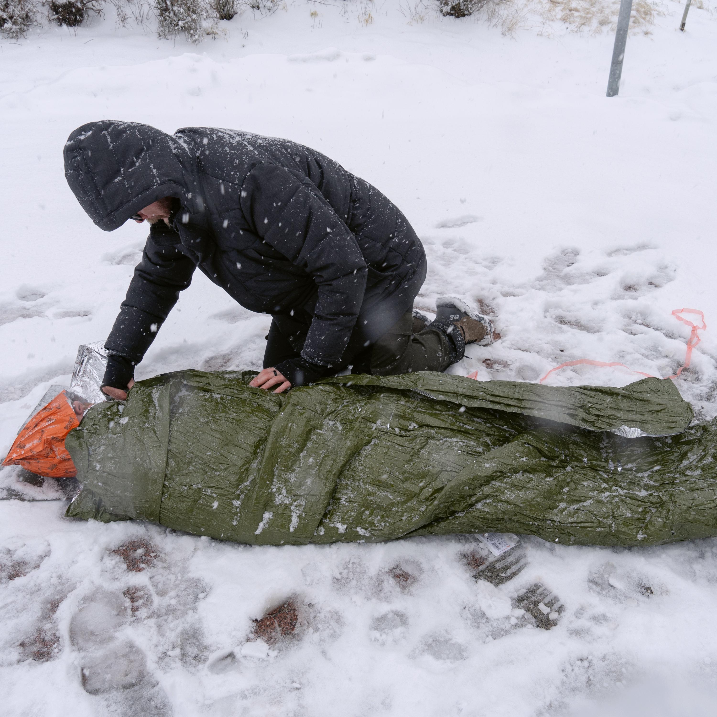 Eine Person bereitet sich in einer Schneelandschaft darauf vor, sich in den grünen Blizzard - Grün, Decke Schlafsack mit mehrlagiger Reflexcell™ Technologie zu legen.