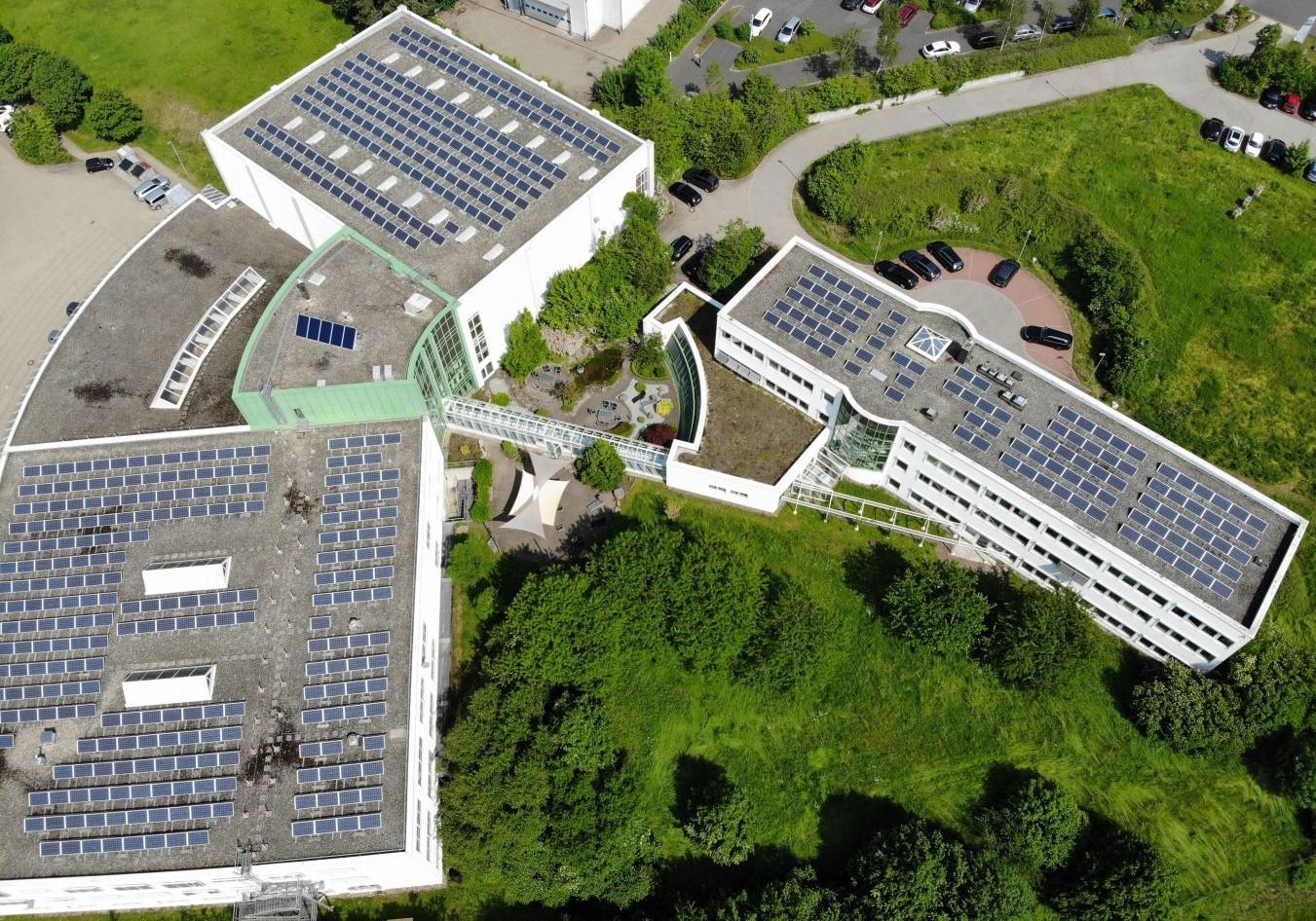 AltText>Moderne Gebäudekomplexe mit Solardächern, begrünten Innenhöfen, Parkplätzen und einem kleinen Teich aus der Vogelperspektive