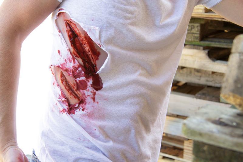 Ein Erler-Zimmer Woundmoulage Schnittwunde groß mit Blutungsfunktion, realistisch auf einem weißen T-Shirt mit künstlichem Blut und großen Öffnungen dargestellt.