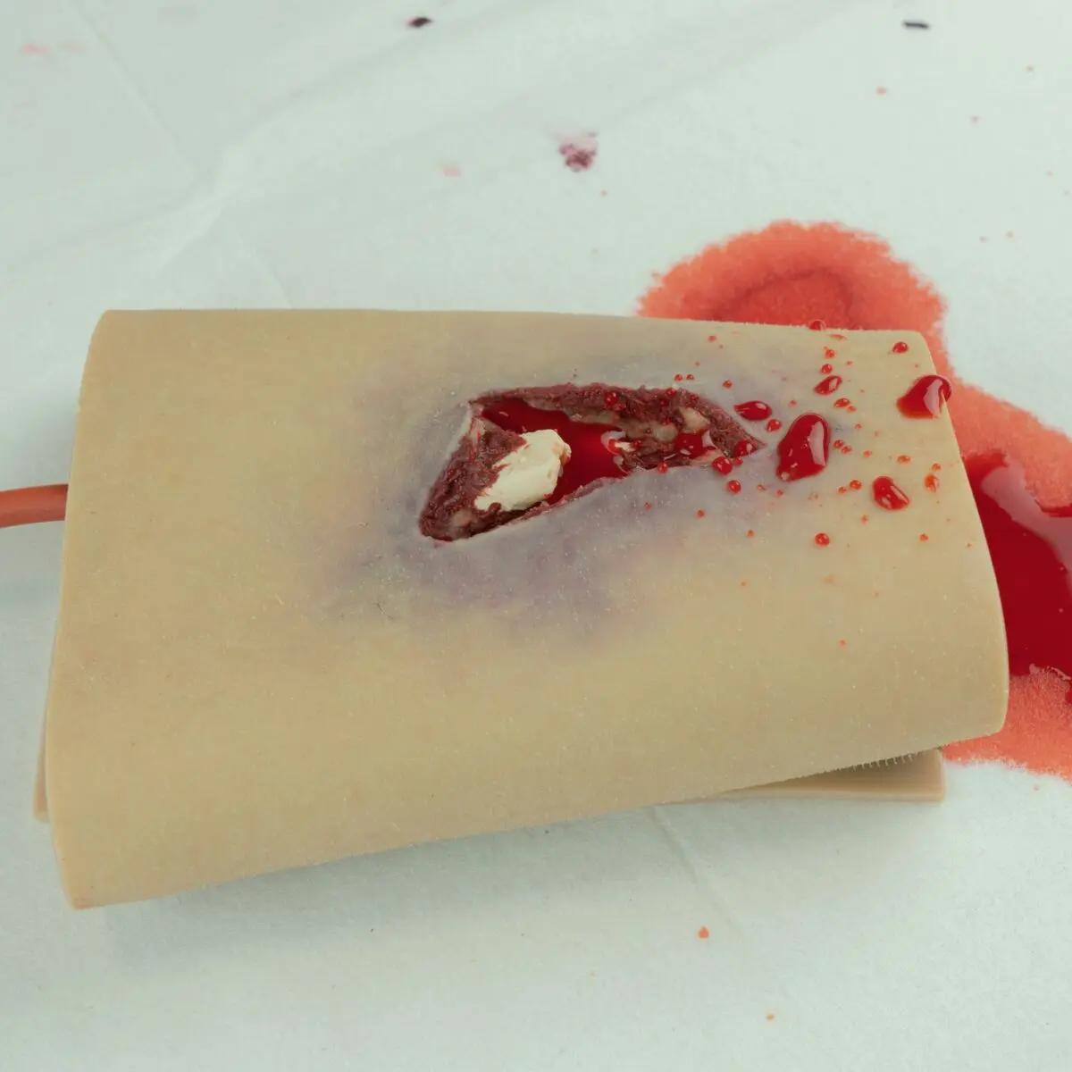Techline Moulage Offene Fraktur-Arm zeigt eine beigen Wundsimulation mit offenem Schnitt, aus dem rote Masse austritt und Gewebe sichtbar ist.