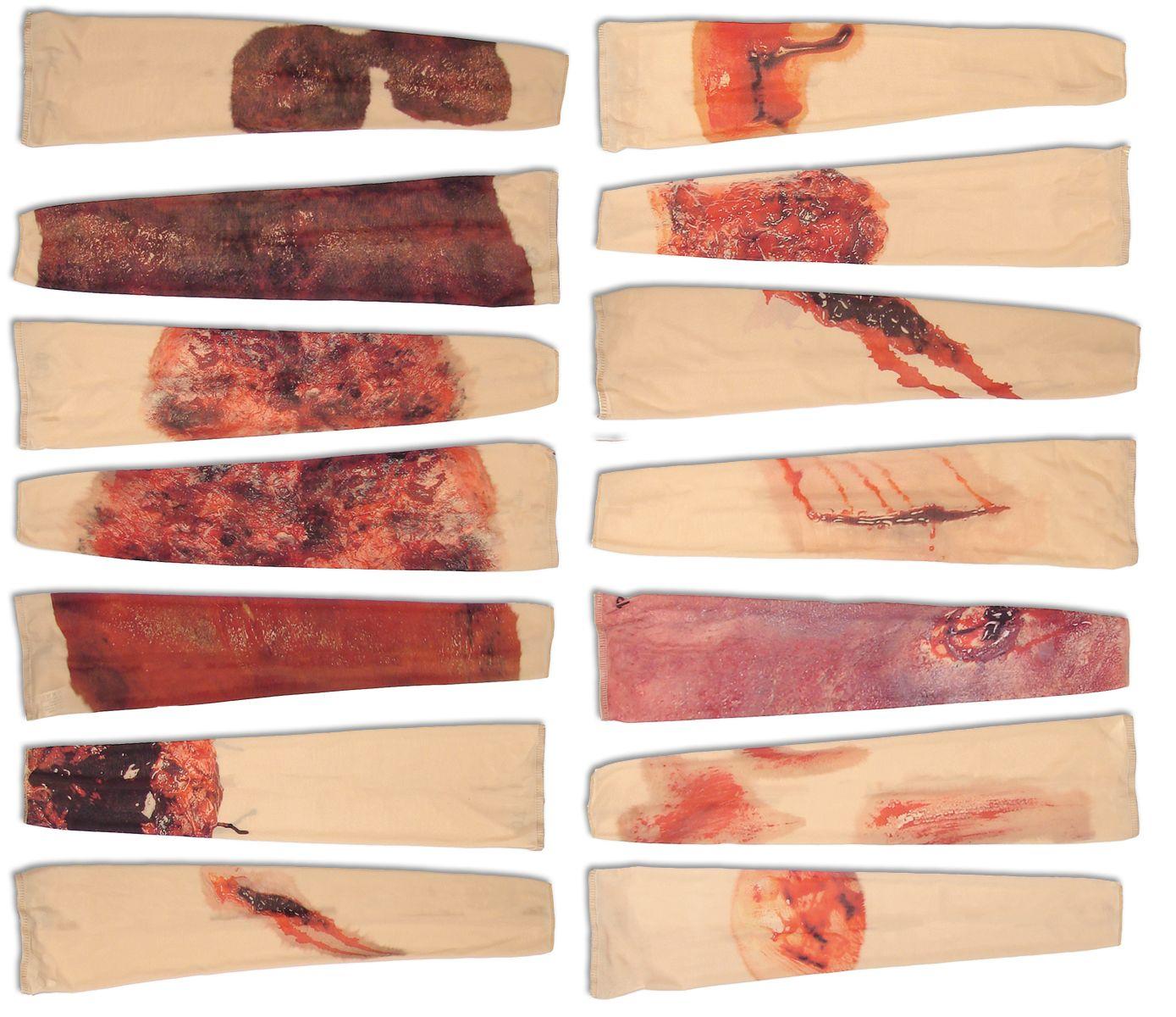 Zwölf RAPID Trauma-Simulation Bandagen mit verschieden gestalteten Schnitt-, Riss- und Schürfwunden liegen in drei Reihen angeordnet.