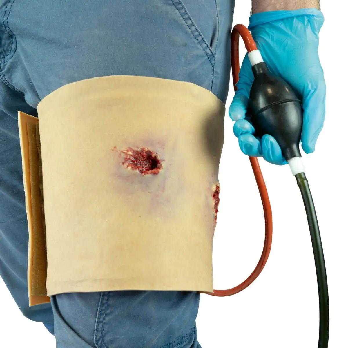 Eine Person trägt die Techline Moulage Schusswunde Bein am Oberschenkel, die eine realistische Schusswunde mit Verbindungskanal simuliert.