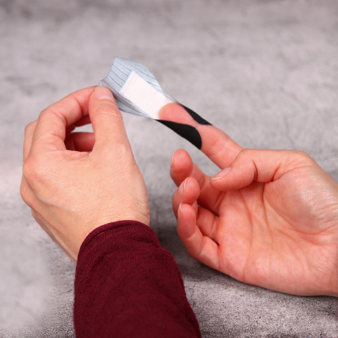 Eine Hand hält ein Weroplast® PowerTex Pflaster - Mini Mix, das aus schwarzem, quer- und längselastischem Textilgewebe besteht und extra starke Klebkraft bietet.