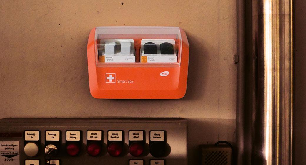 WERO Smart Box Orange mit transparenter Abdeckung, zeigt zwei Steckplätze für Netzadapter, montiert über einem grauen Schaltschrank mit Bedienelementen.