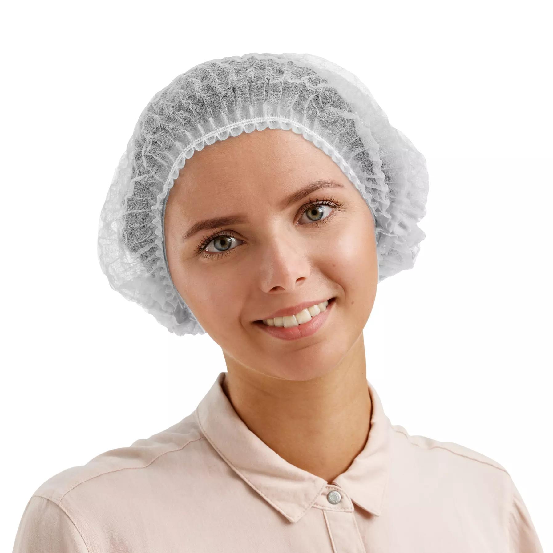 Eine lächelnde Frau trägt eine weiße Einweghaube, 100 Stk - Weiß, nicht detektierbar, atmungsaktive Kopfbedeckung für Hygienebereiche.