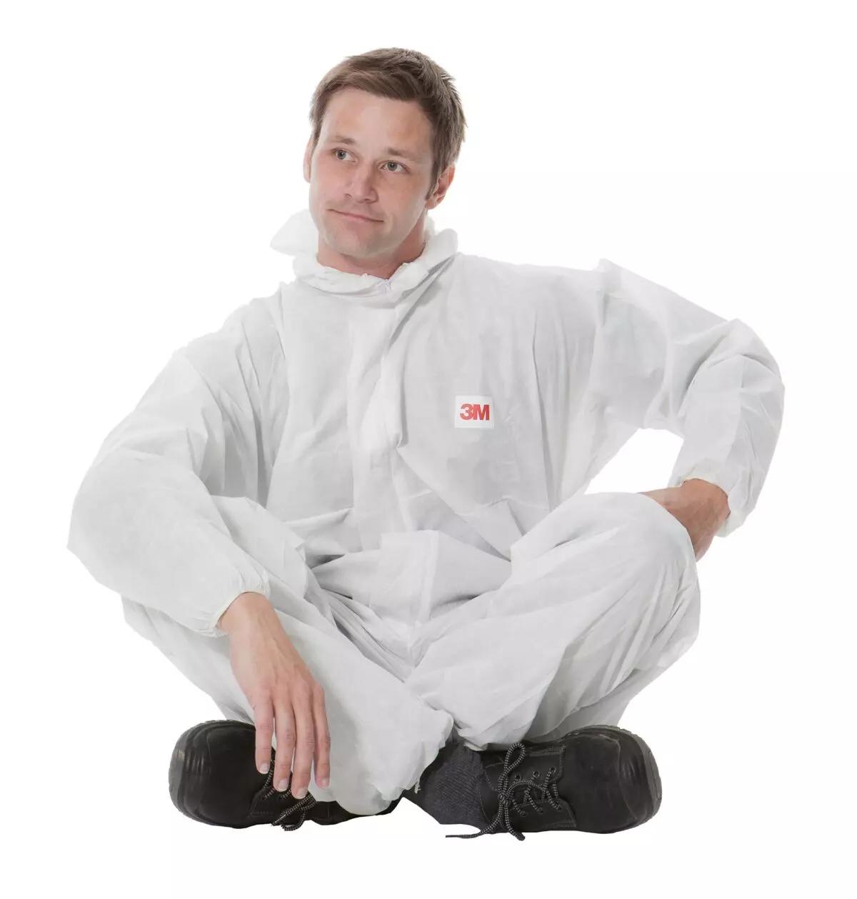 Ein Mann trägt den 3M™ Schutzanzug 4515 - XL aus weißem SMS-Polypropylen, sitzt entspannt mit gekreuzten Beinen und zeigt das 3M Logo.