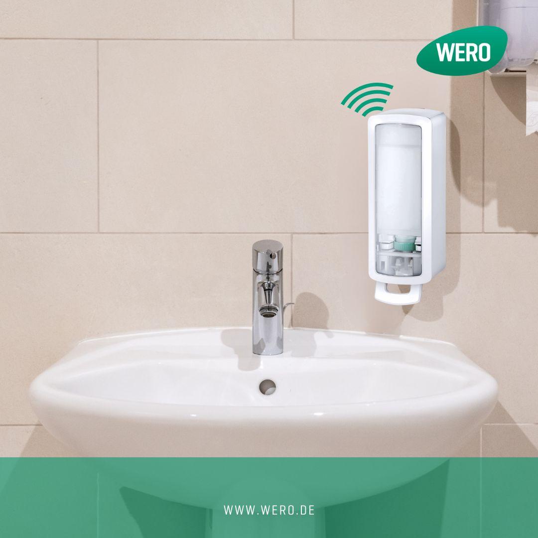 Weißes Waschbecken mit silbernem Wasserhahn, wandmontierter weißer Seifenspender, WERO Logo und grünem Kabel im Badezimmer.