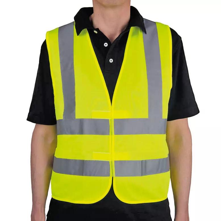 Eine Person trägt eine Warnweste nach DIN EN ISO 20471:2013 / Klasse 1 mit verstellbarem Klettverschluss und zwei reflektierenden Streifen.