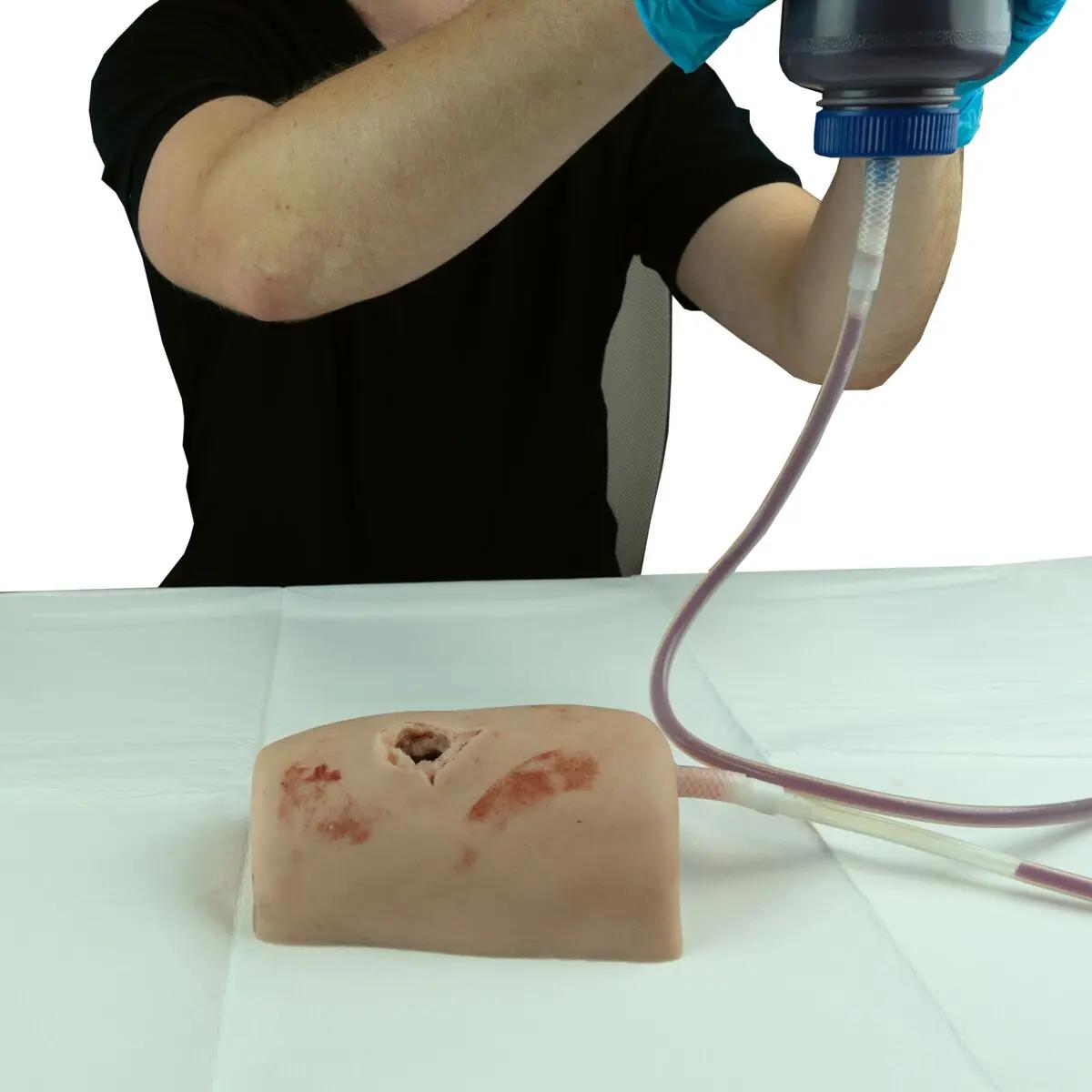 Eine Person übt mit dem TrueClot® Wound Packing Task Trainer Schusswunden das Realitäts-nahe Stopfen einer simulierten Schusswunde mit blutähnlicher Flüssigkeit.