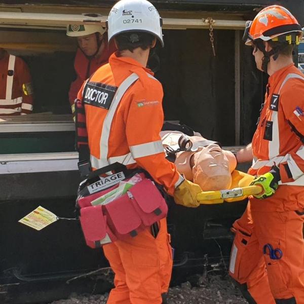 Notfallhelfer in orangefarbener Schutzkleidung nutzen das SmartTriage™ Tri Pack mit abnehmbaren Schultergurten bei einer Triage-Übung mit Trage.