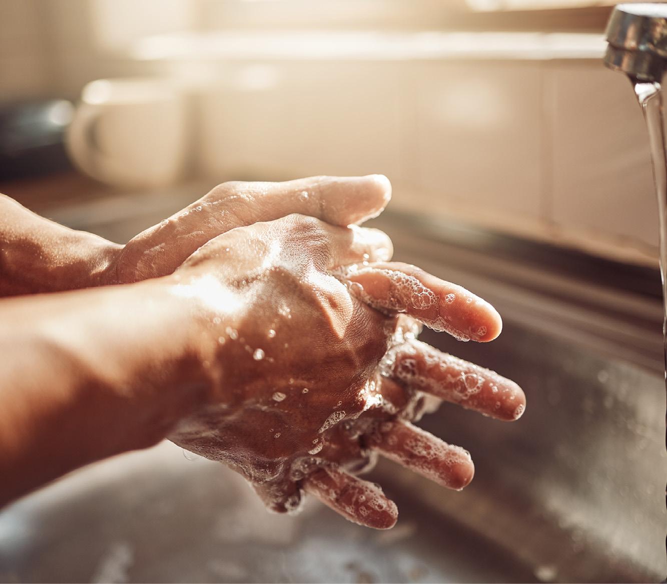 Zwei fairhäutige Hände werden unter fließendem Wasser mit Seife gründlich am Küchenwaschbecken gereinigt.