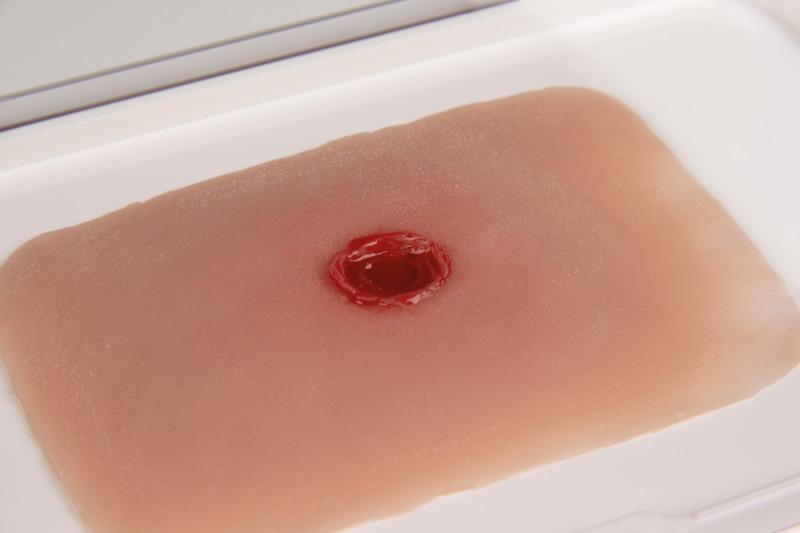 Erler-Zimmer Woundmoulage Einschusswunde mit rundem künstlichen Einschussloch und simuliertem Blutaustritt zur realistischen Verletzungsdarstellung.