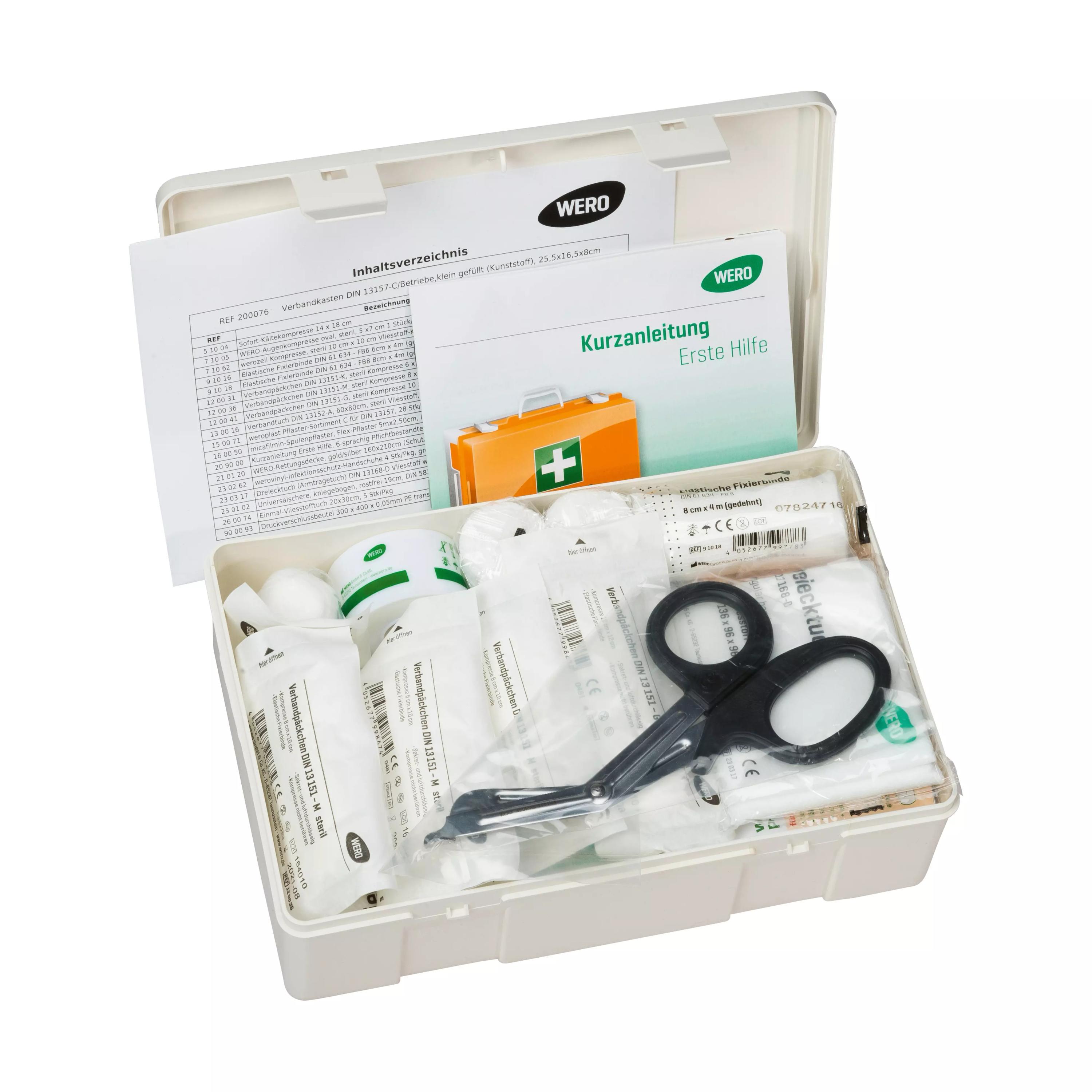Ein geöffneter WERO Verbandkasten DIN 13157-C mit umfassender Erste-Hilfe-Ausstattung, darunter verschiedene sterile Verbandmaterialien, eine Universalschere und bebilderte Kurzanleitung.