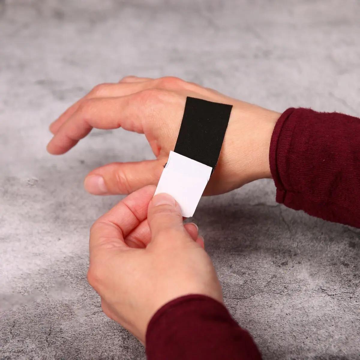 Eine Hand fixiert einen schwarzen Wundschnellverband Weroplast® PowerTex - 6 cm, 5 m mit verstärkter Klebkraft am Handgelenk.