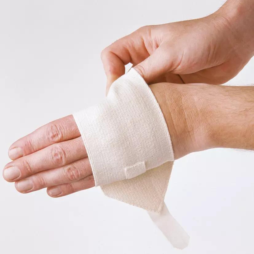 Zwei Hände wickeln eine WERO Sanit® Handgelenkbandage in Beige, Größe M, aus starkem Elastik-Baumwollgewebe um ein rechtes Handgelenk.