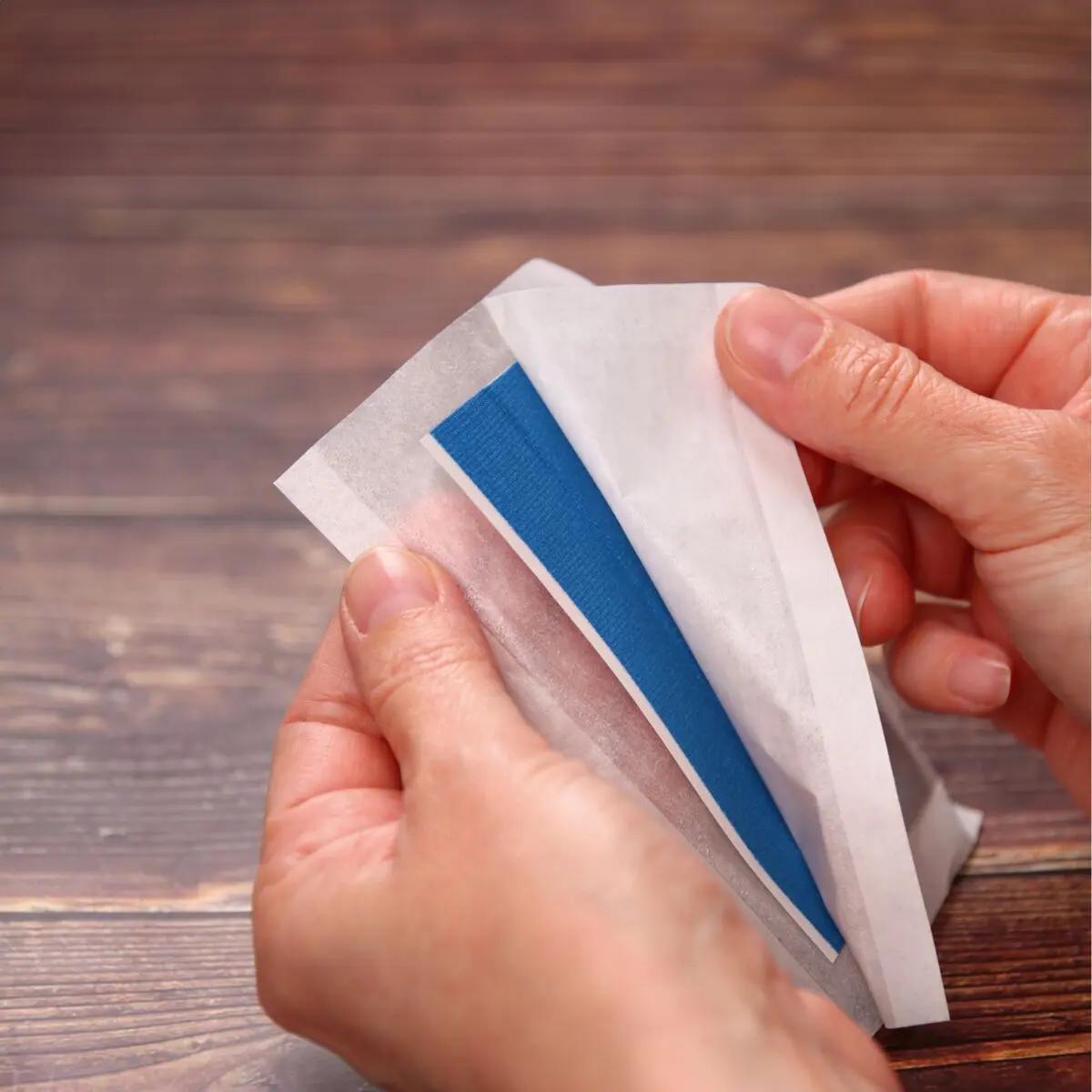 Zwei Hände halten ein blaues Pflaster aus dem Pflasterset Weroplast® PowerDetect - Nachrüst-Set DIN 13157 - 2021 mit Aluminiumstreifen und elastischem Gewebe.