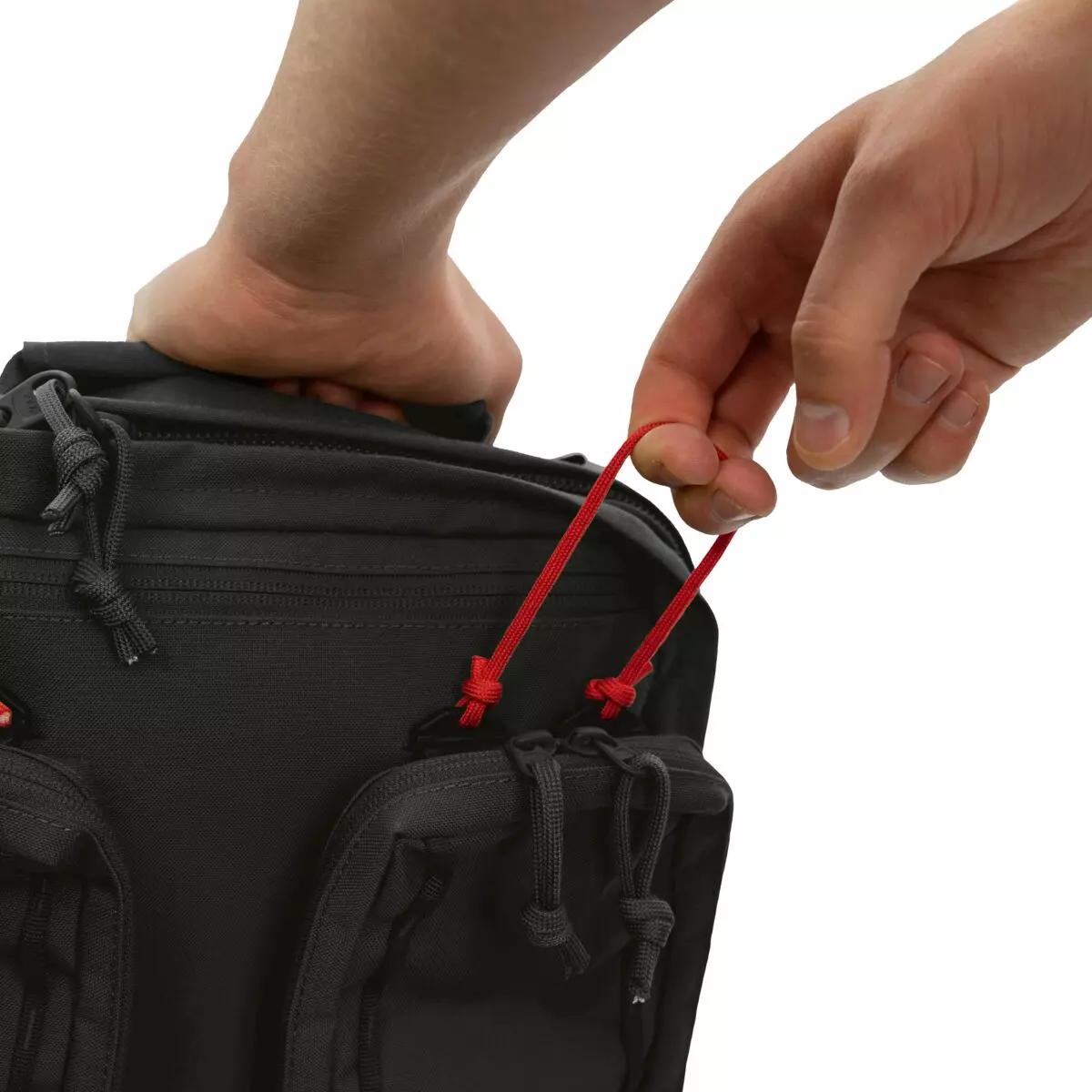 Eine Hand hält eine rote Kordel am TT Medic Mascal Pack - Schwarz, der Rucksack mit zwei Reißverschlusstaschen und vier IFAK-Pouches zeigt.
