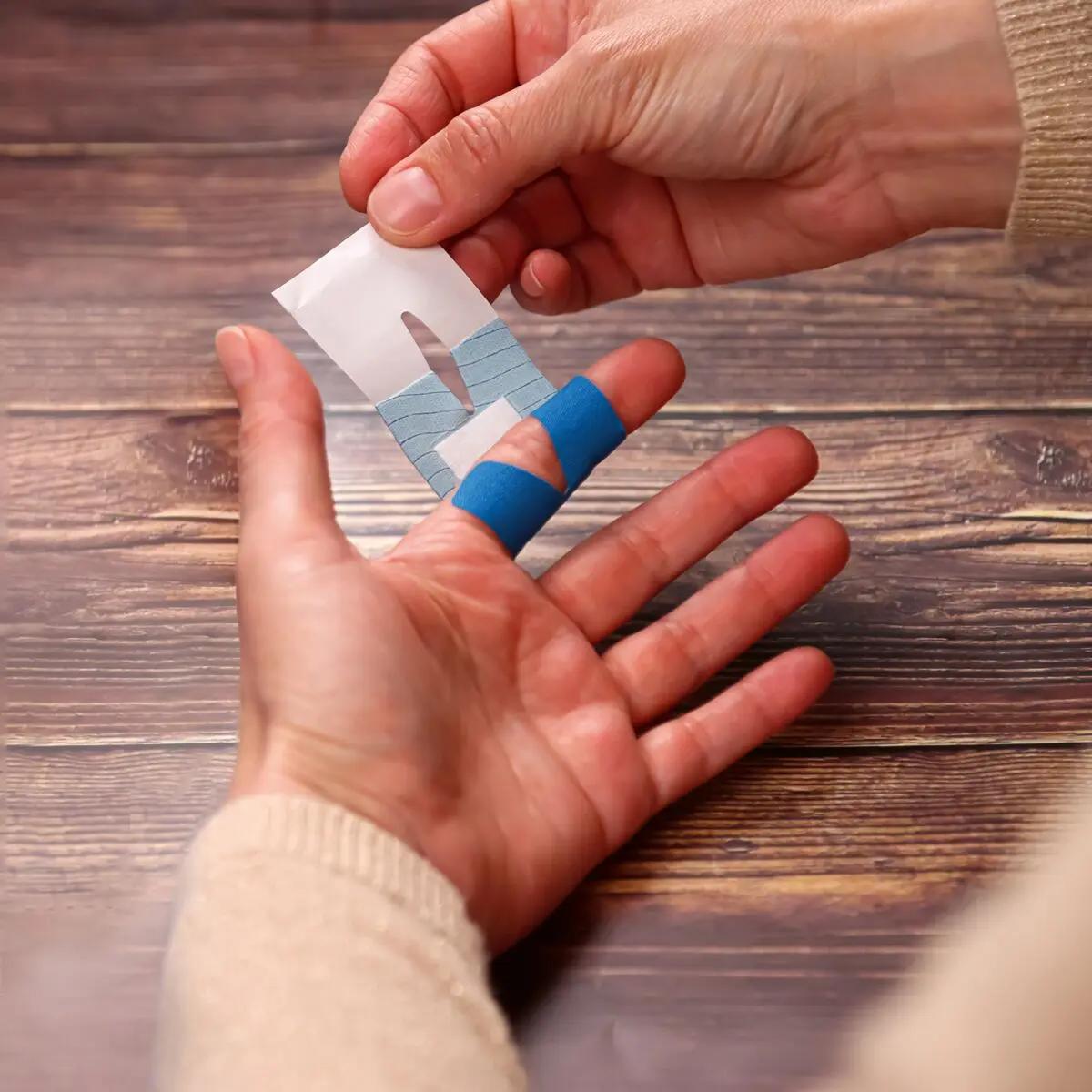 Eine Hand hält ein weißes Papier, während die andere ein Pflasterset Weroplast® PowerDetect - Perfect Mix Fingerpflaster mit blauer, detektierbarer Oberfläche anlegt.