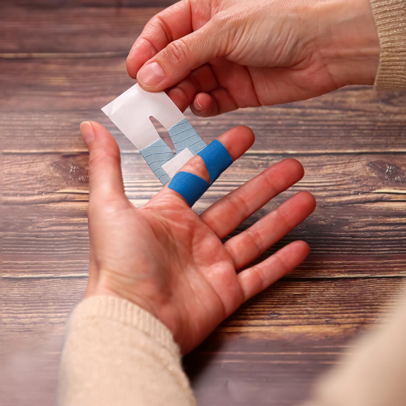 Eine Hand hält ein weißes Papier, während die andere ein Pflasterset Weroplast® PowerDetect - Perfect Mix Fingerpflaster mit blauer, detektierbarer Oberfläche anlegt.